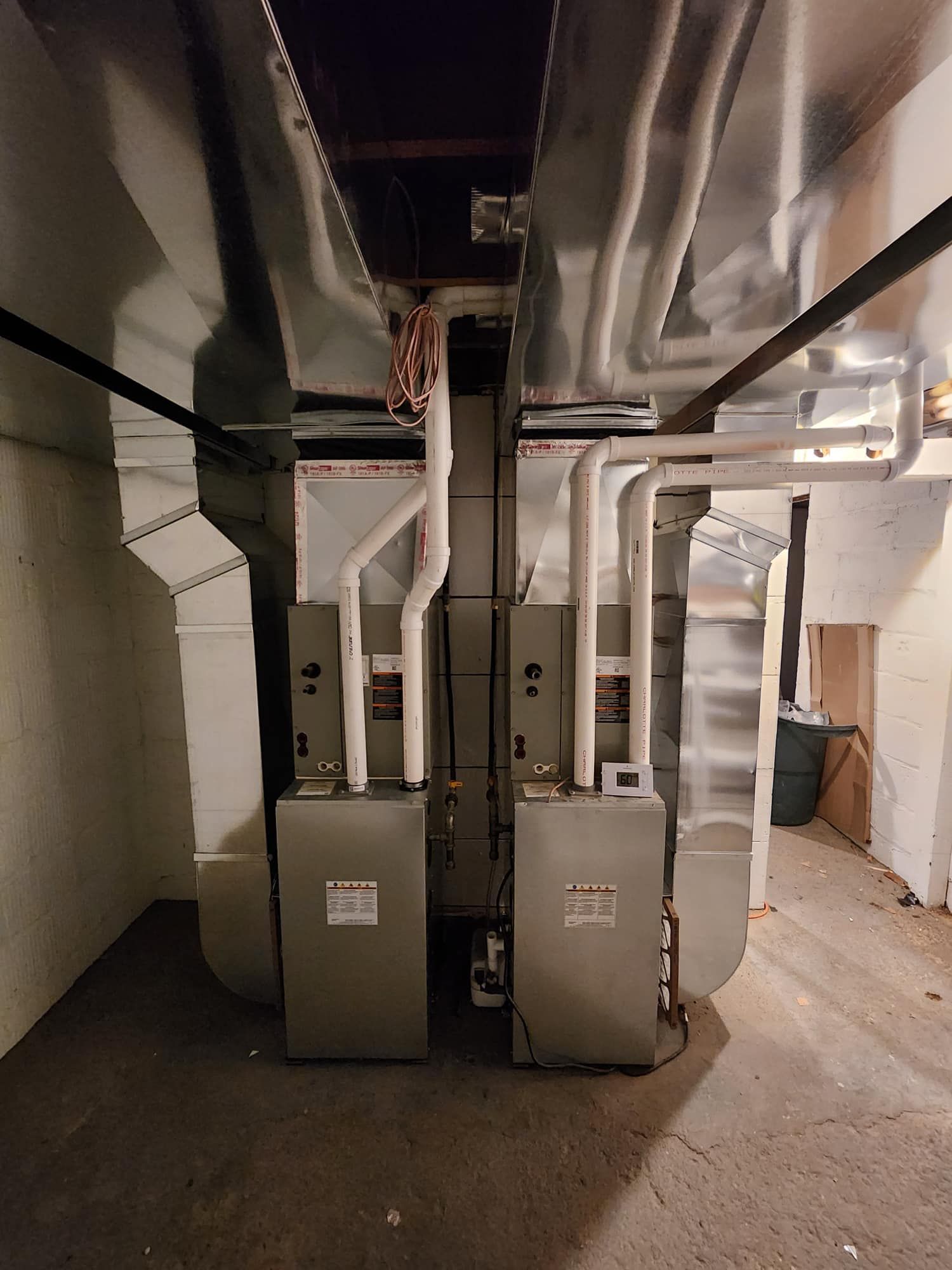 Two silver HVAC units with ductwork in a basement setting.