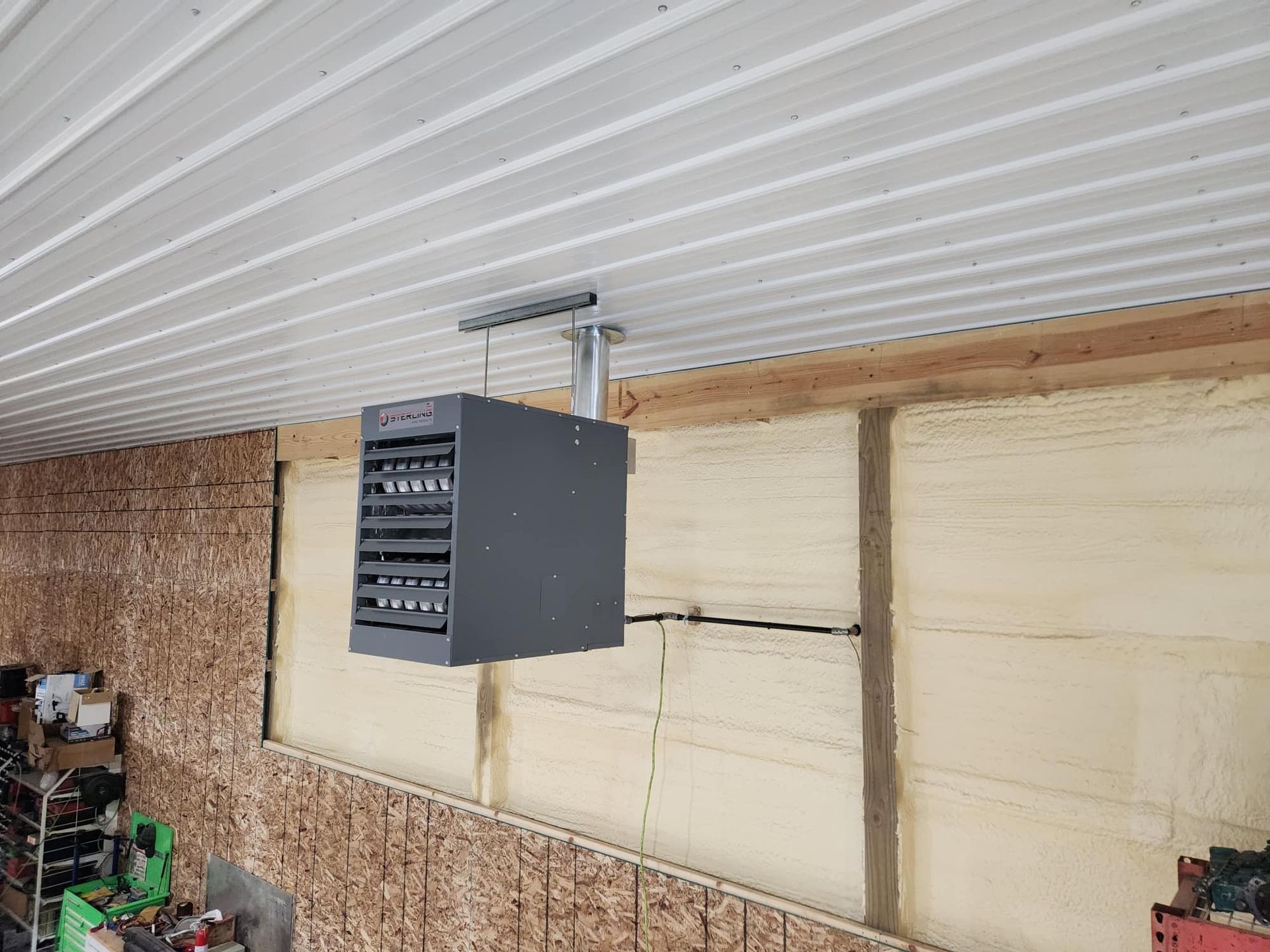 Gray industrial heater suspended from a corrugated metal ceiling. 