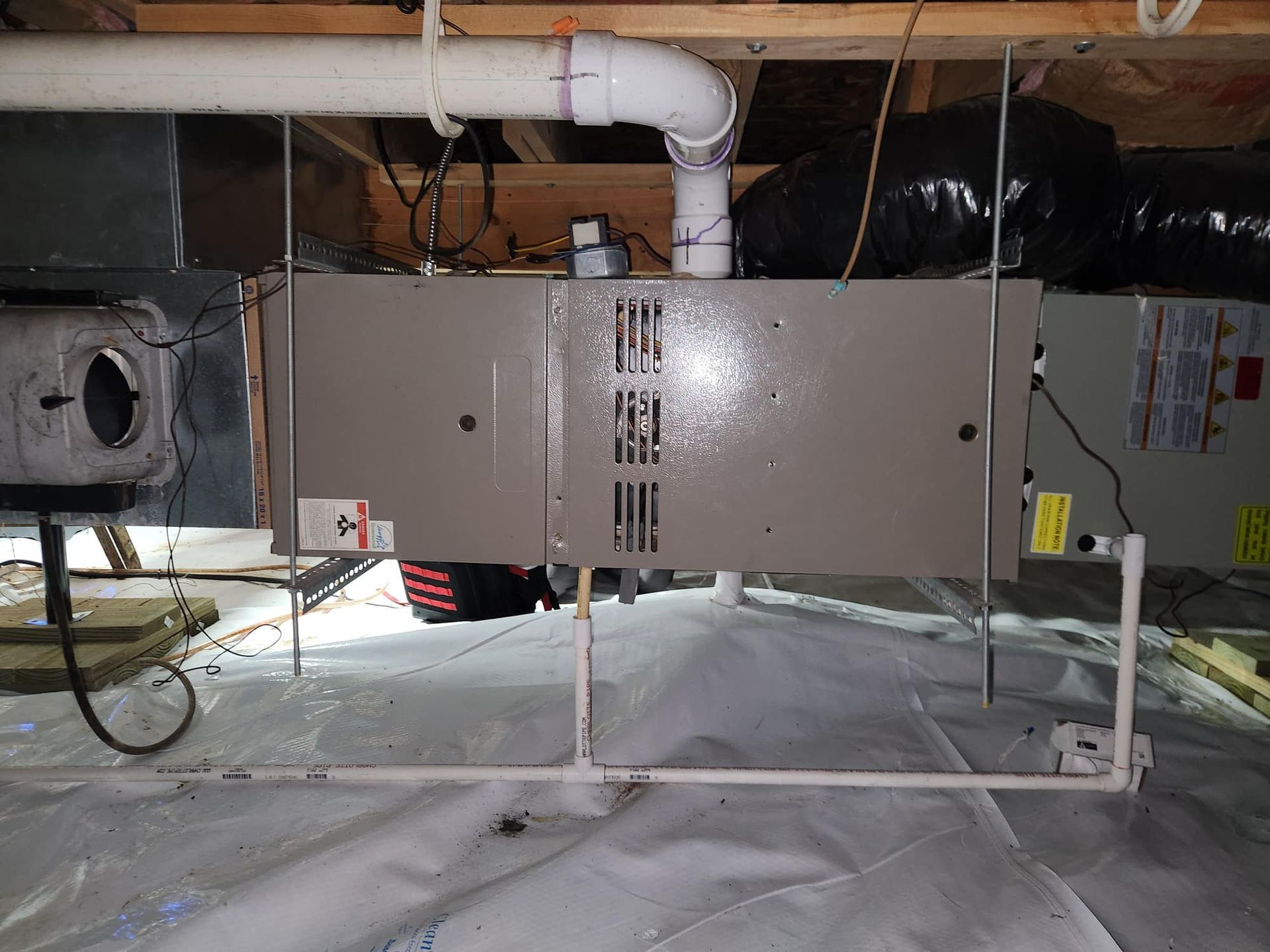Furnace in a crawl space, with ductwork, pipes, and wiring visible.