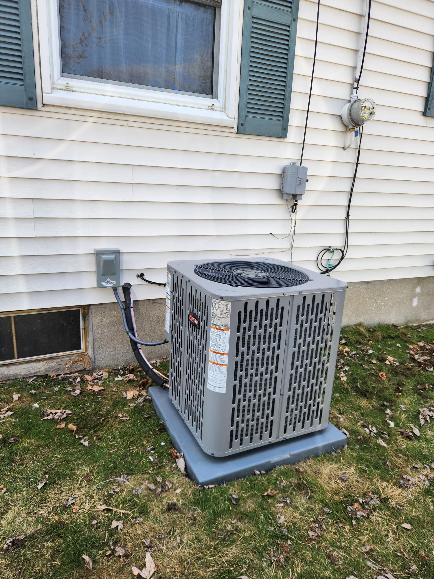 Air conditioning unit on a concrete pad outside a white house with shutters.