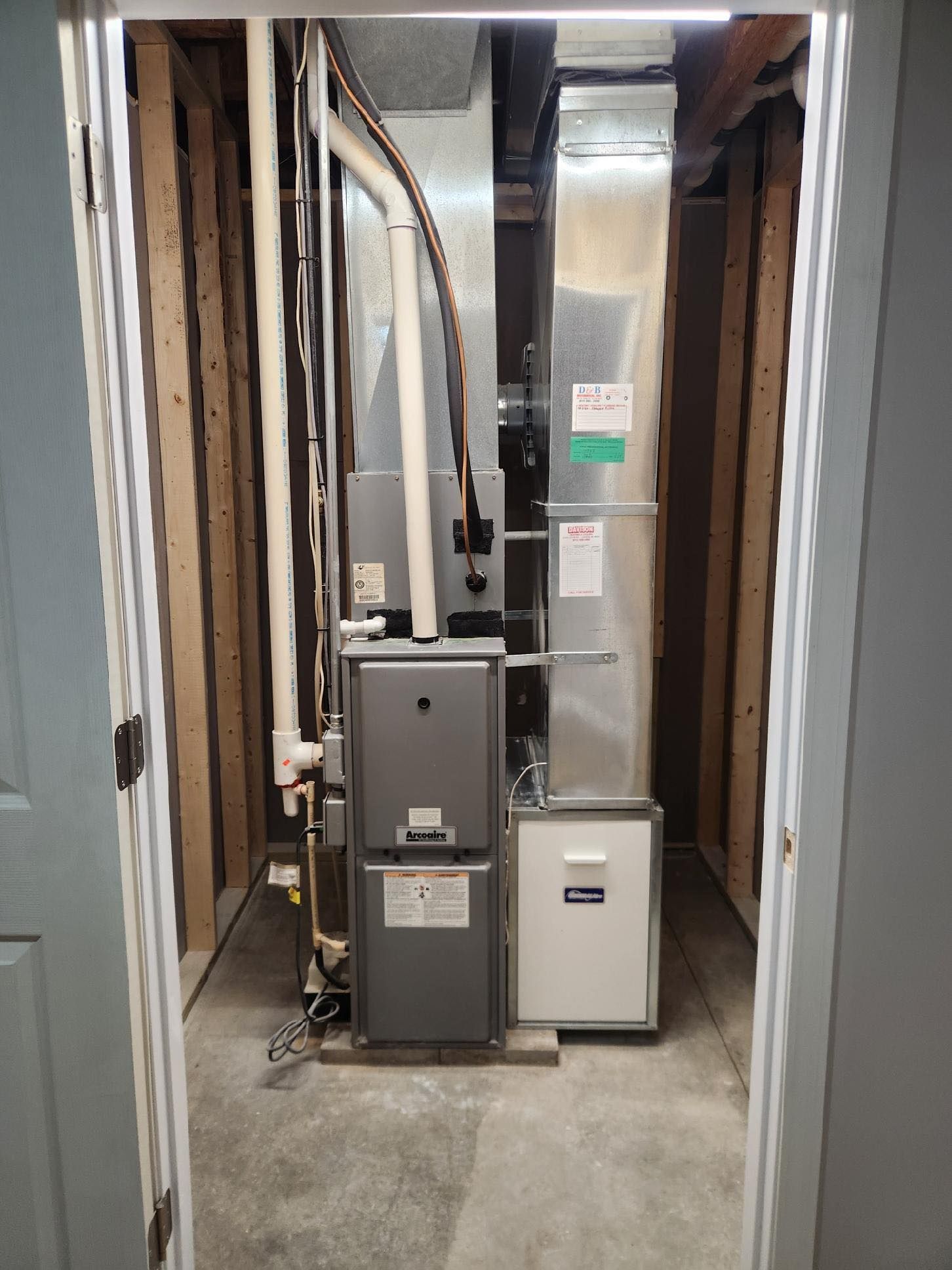 Furnace and air handler in a closet, with ductwork and piping visible.