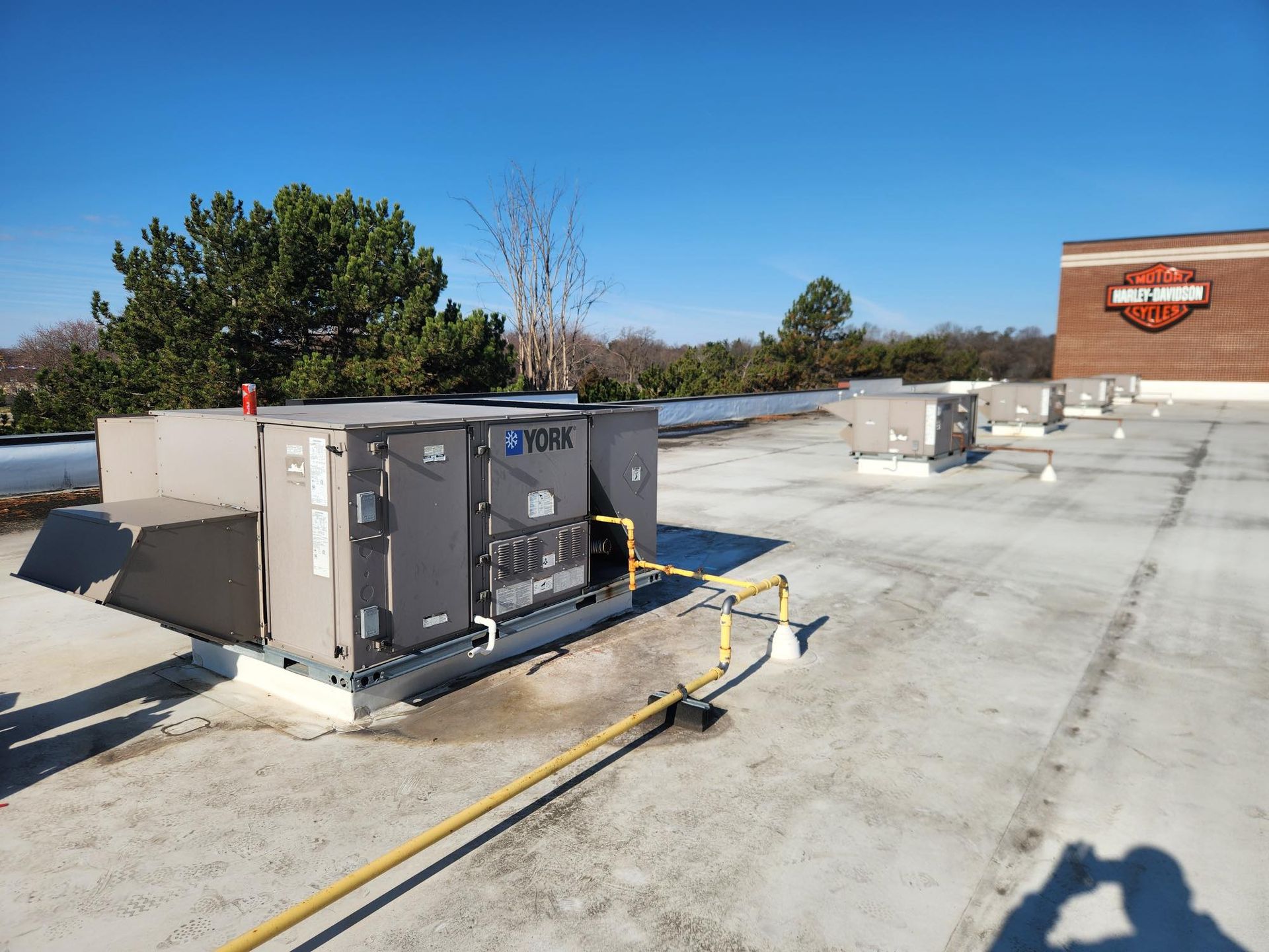 Rooftop with HVAC units under a clear, sunny sky, near a building with a Harley-Davidson logo.