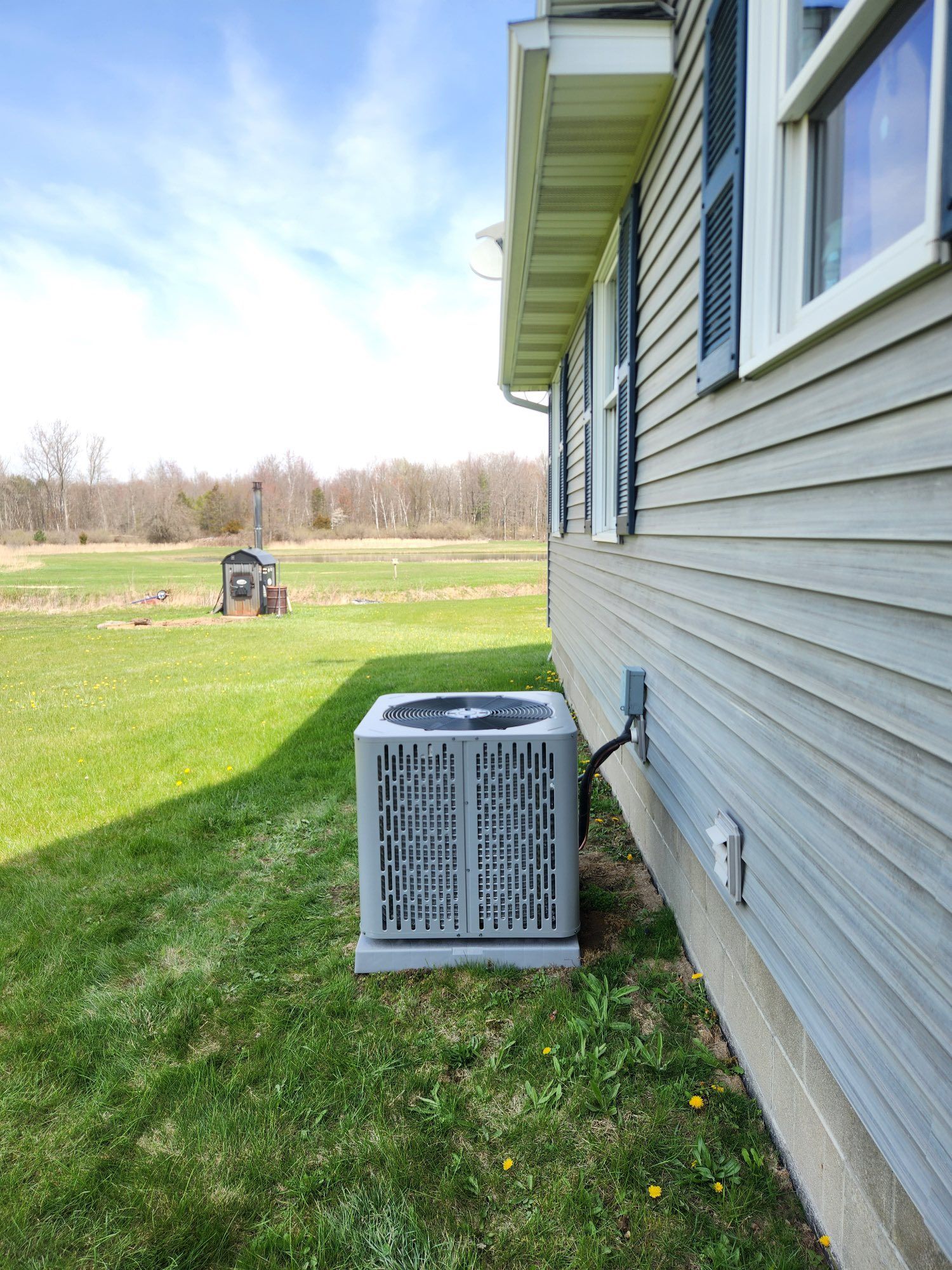 Air conditioner unit next to a light gray house with green grass in front.
