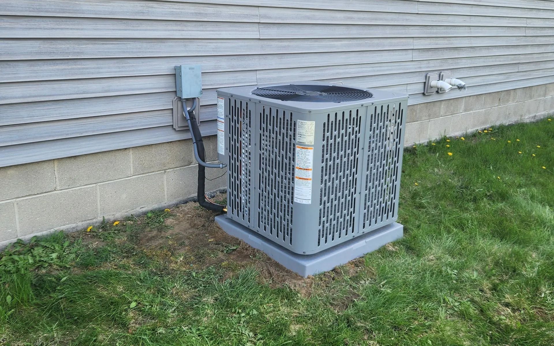 Air conditioner unit outside a building, gray and rectangular, with electrical box and gray siding.