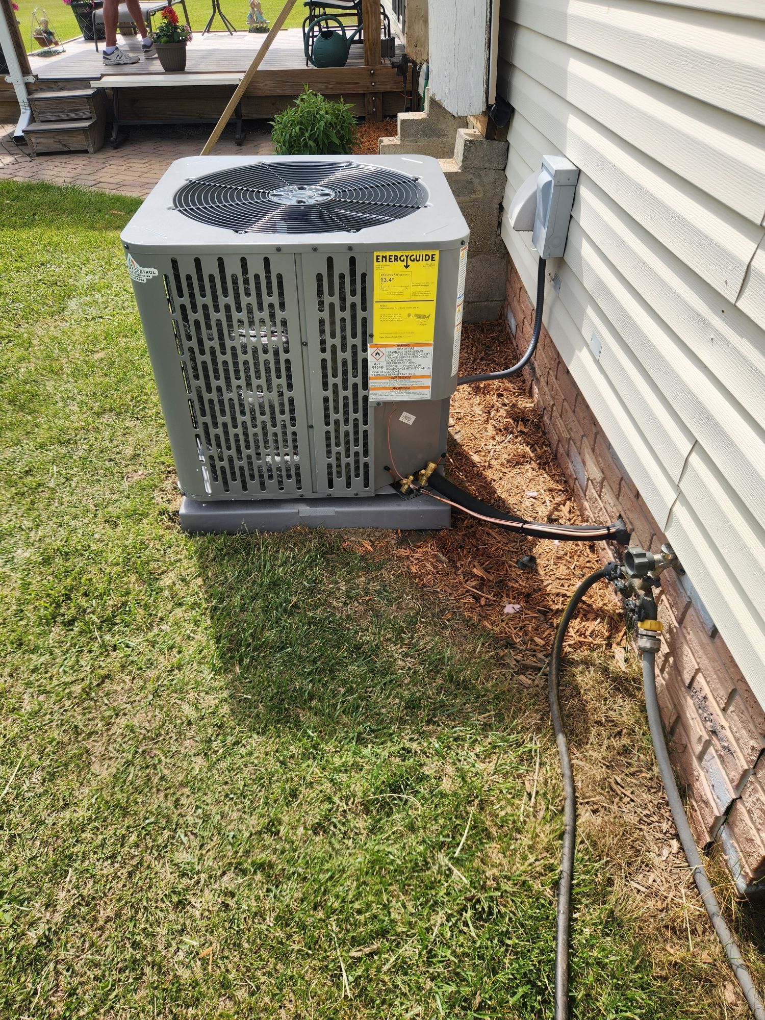 Outdoor air conditioning unit next to a house with a power connection and garden.