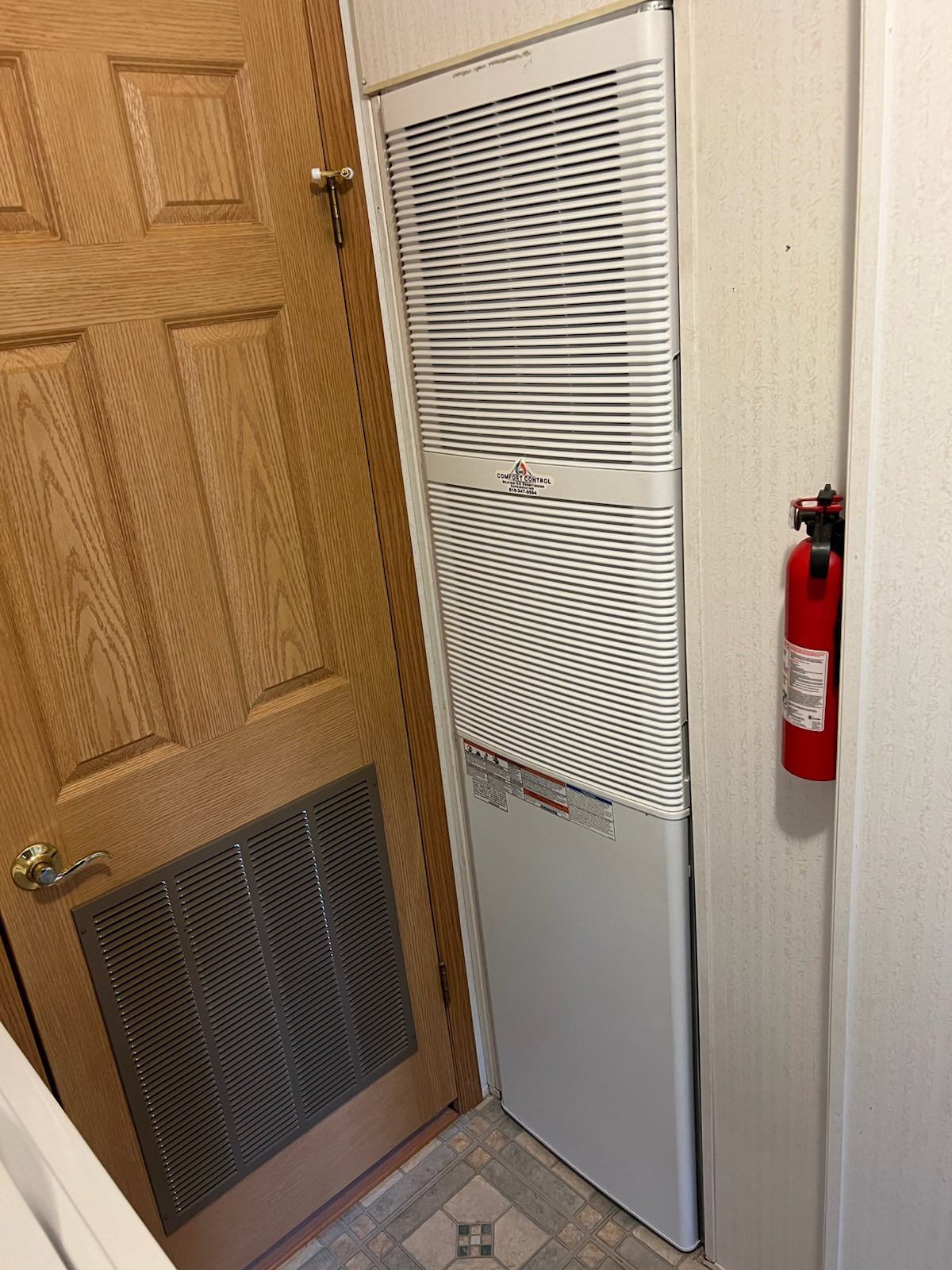 A utility closet with a white air handler, wooden door, and a red fire extinguisher.