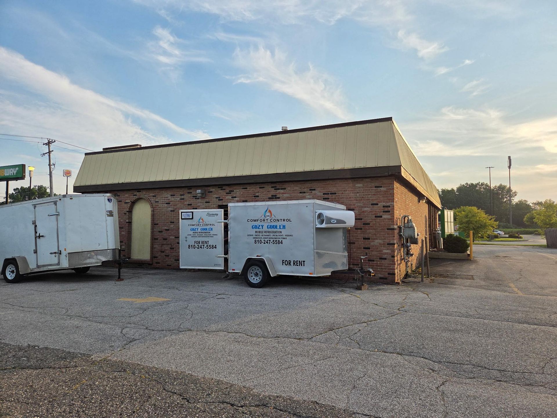 Brick building with open white trailer and another trailer parked next to it. Exterior shot.