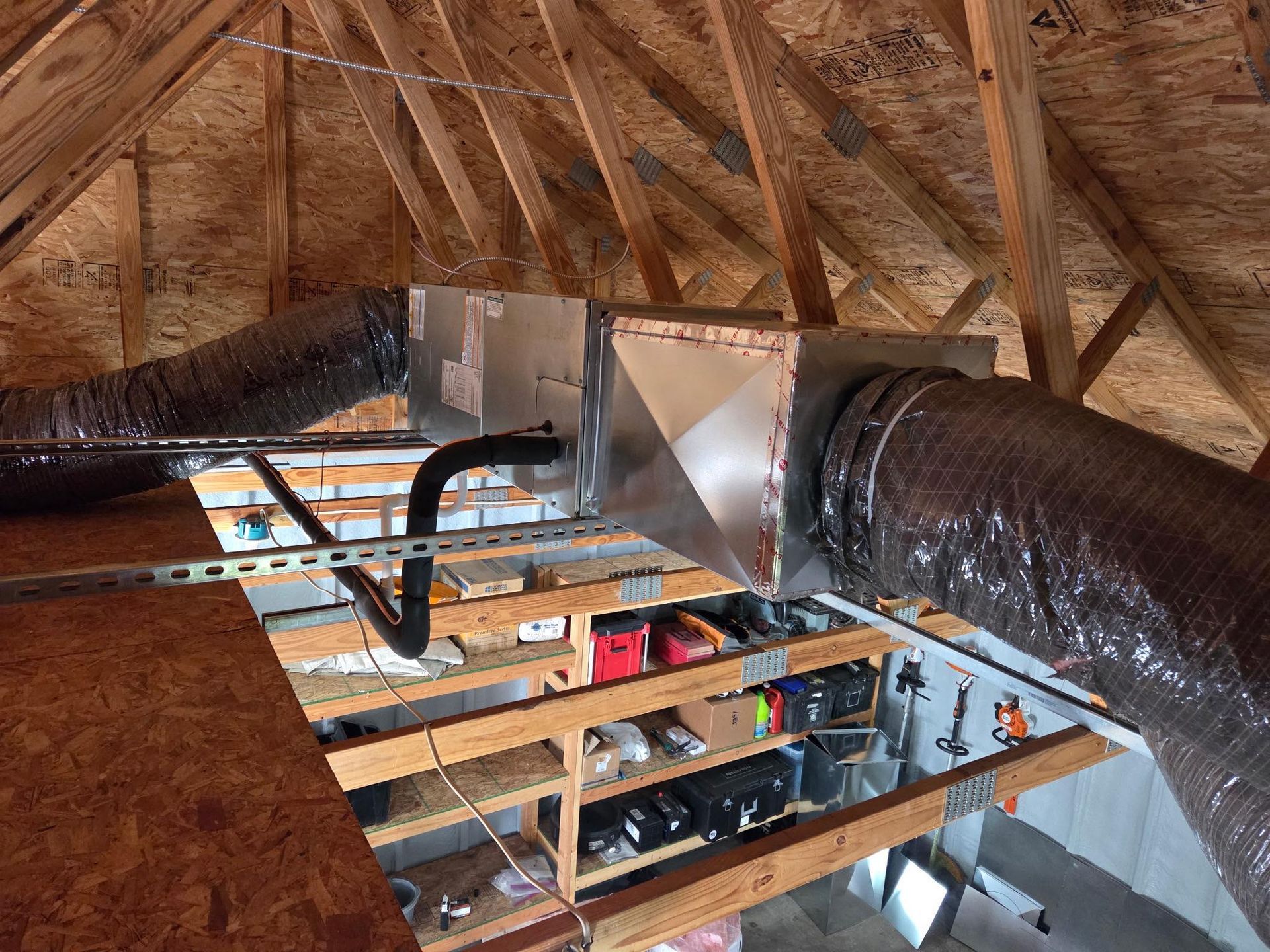 HVAC system in attic: metal boxes, insulated flexible ducts, wooden beams, storage shelves.