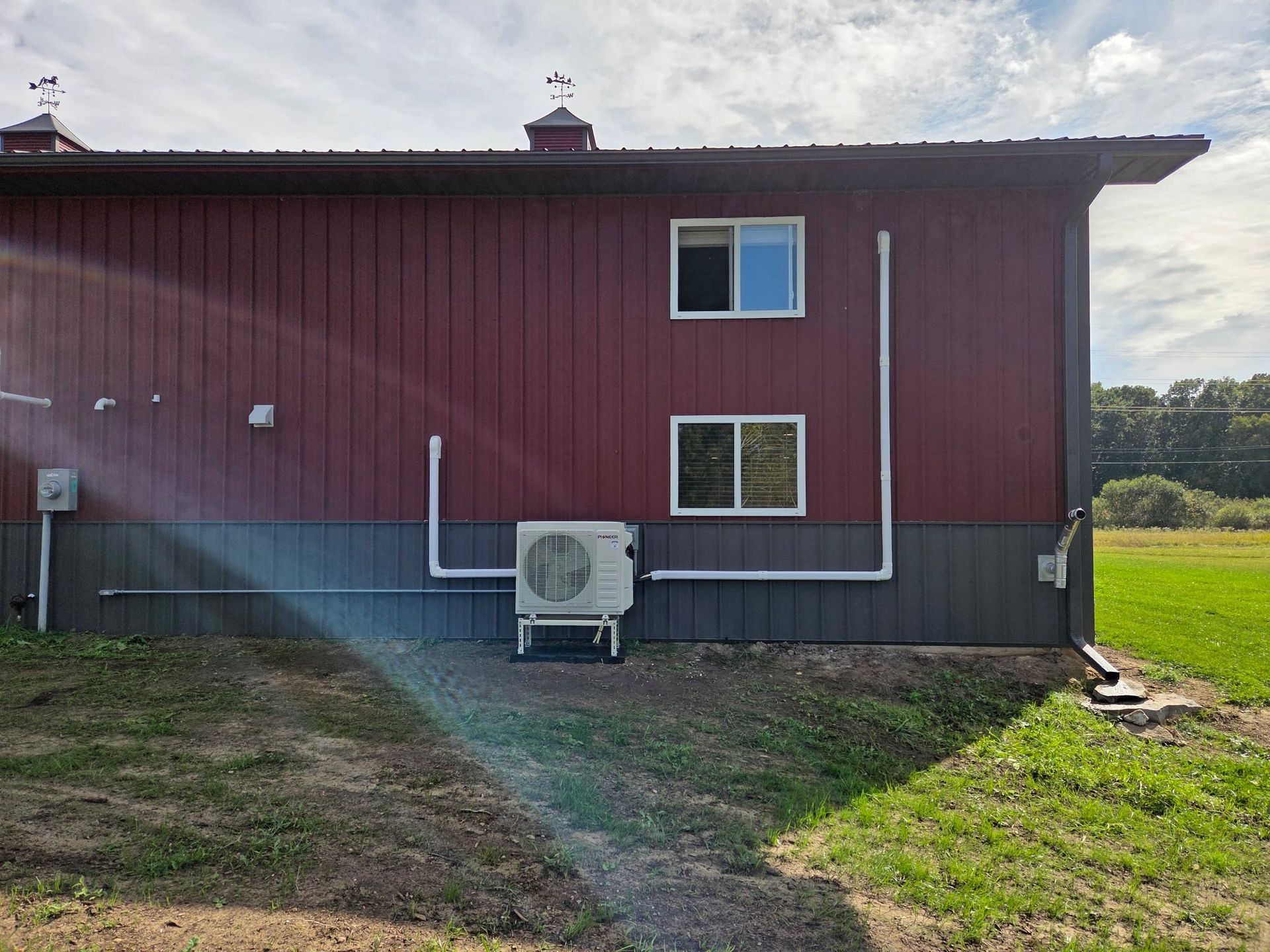 Side of a red and gray barn with an air conditioning unit and white pipes.