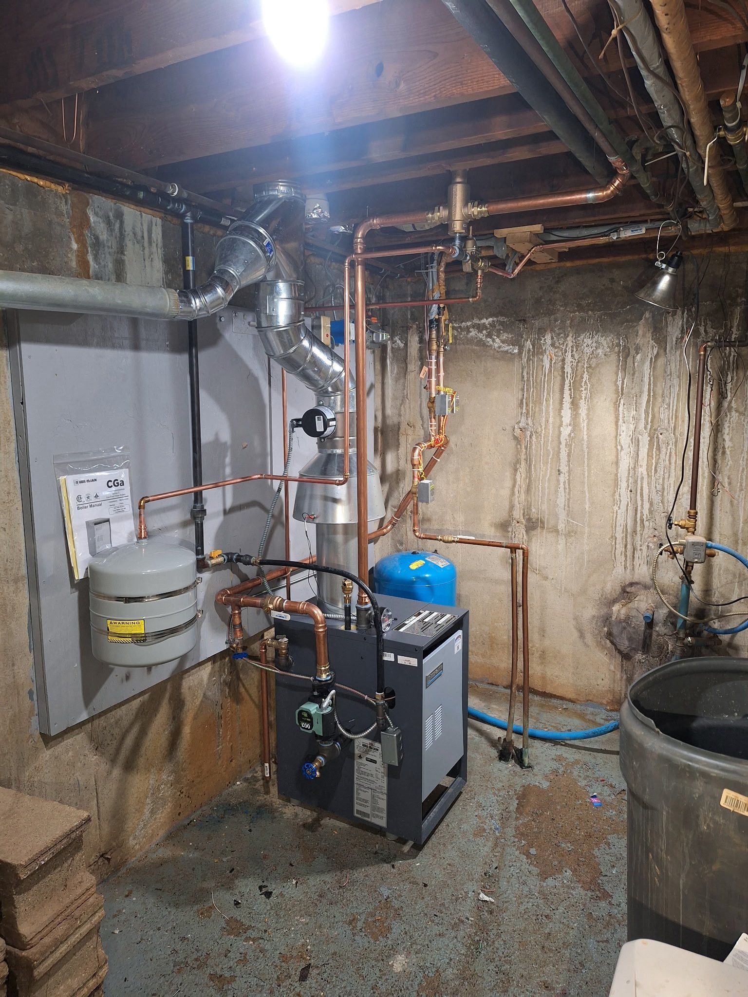 A basement with a heating system, pipes, and a water tank. Gray and copper pipes against a concrete wall.