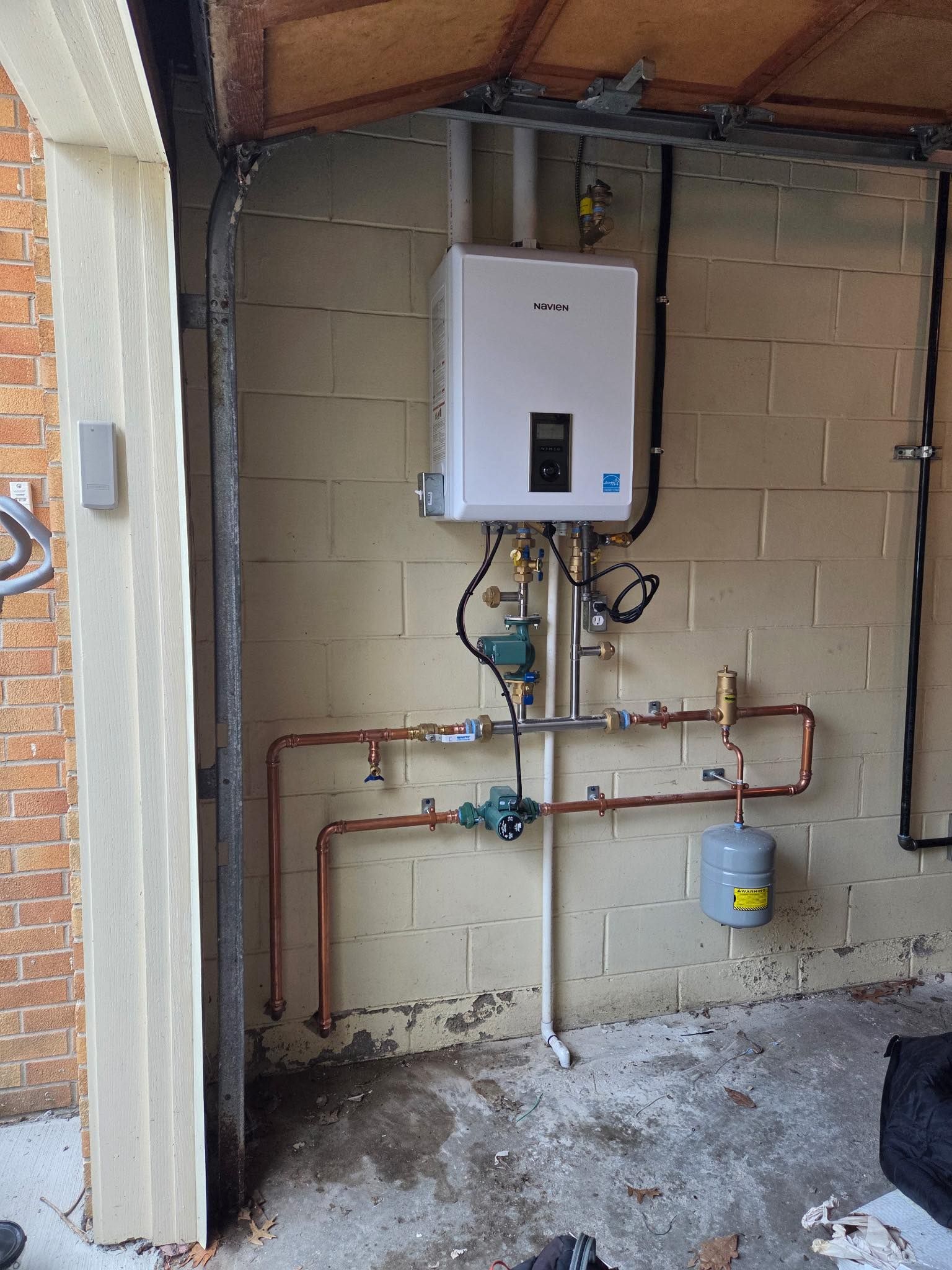 A gas water heater installed on a beige garage wall with copper pipes.