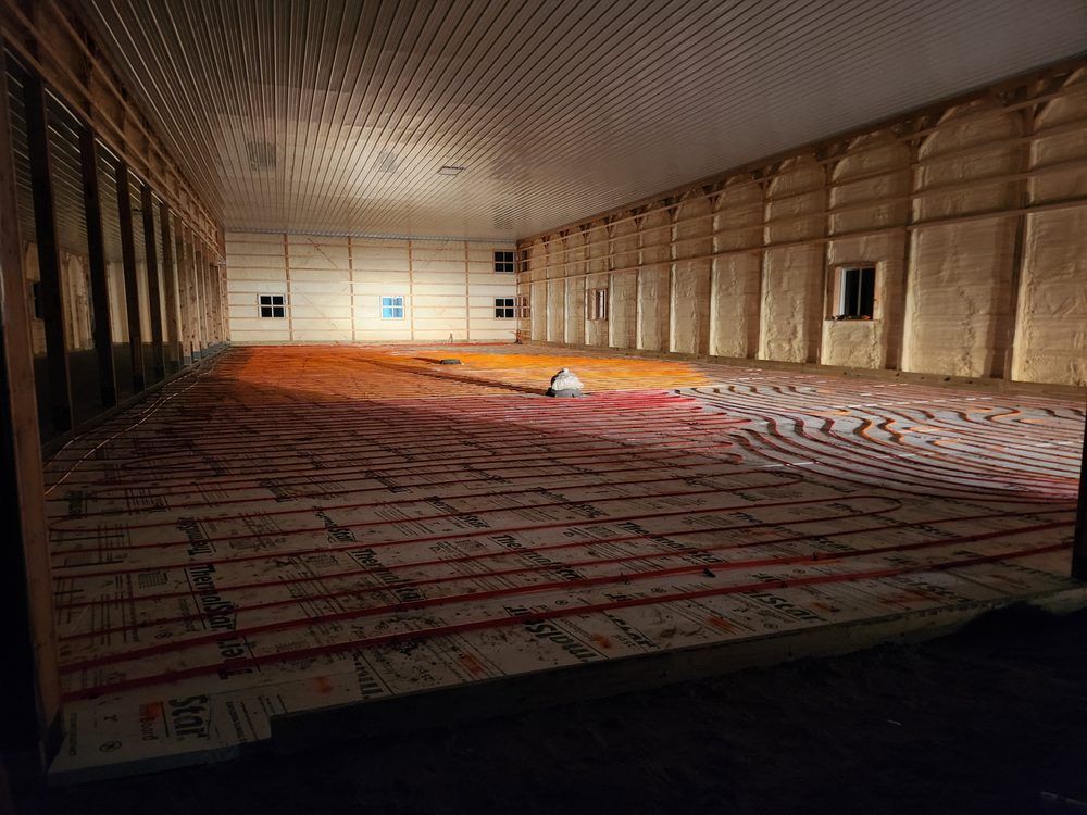 Interior of a large building, possibly a barn, with a radiant floor heating system visible. 