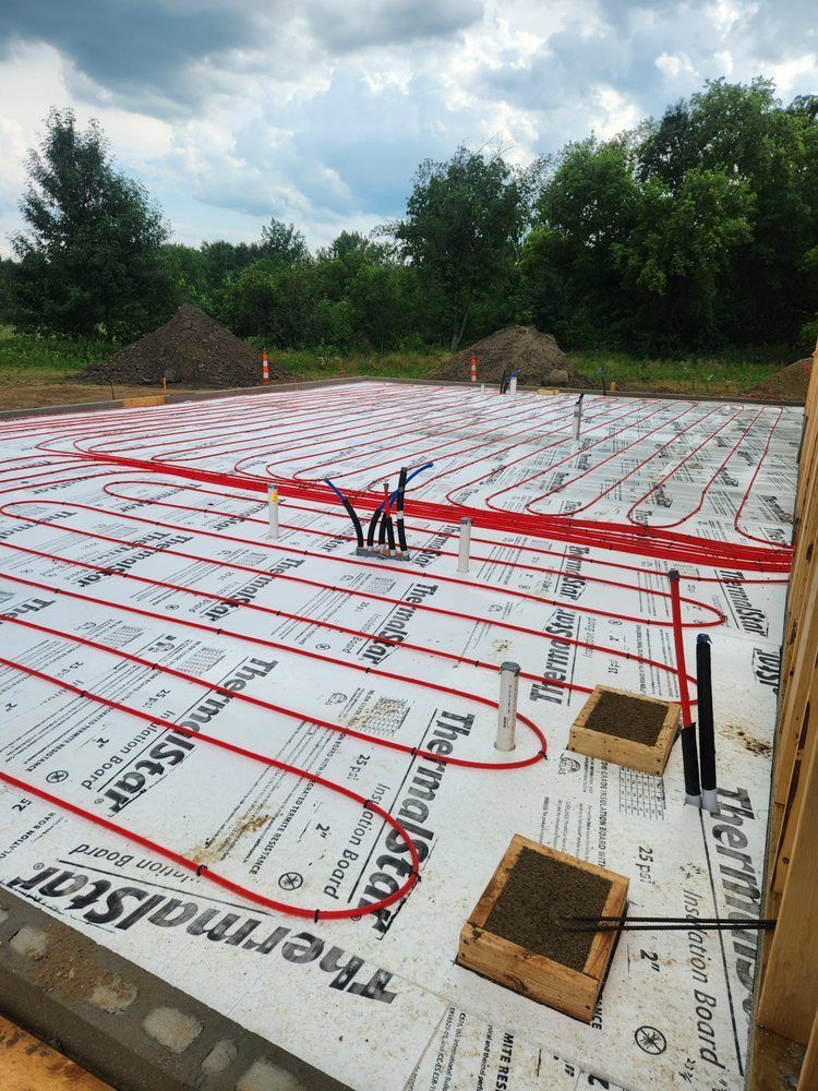 Red radiant floor tubing laid on white insulation, ready for concrete pour at a construction site.