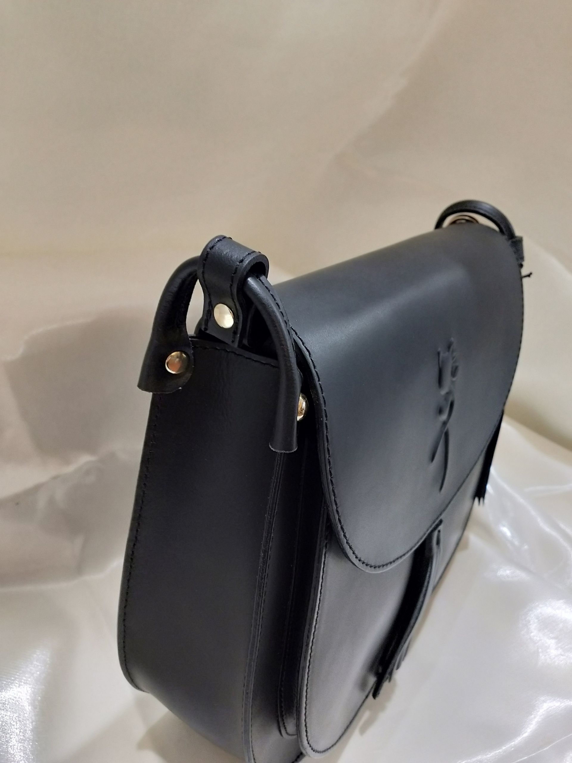 Vista laterale di una borsa a tracolla in pelle nera con cuciture a vista e rivetti in metallo argentato.