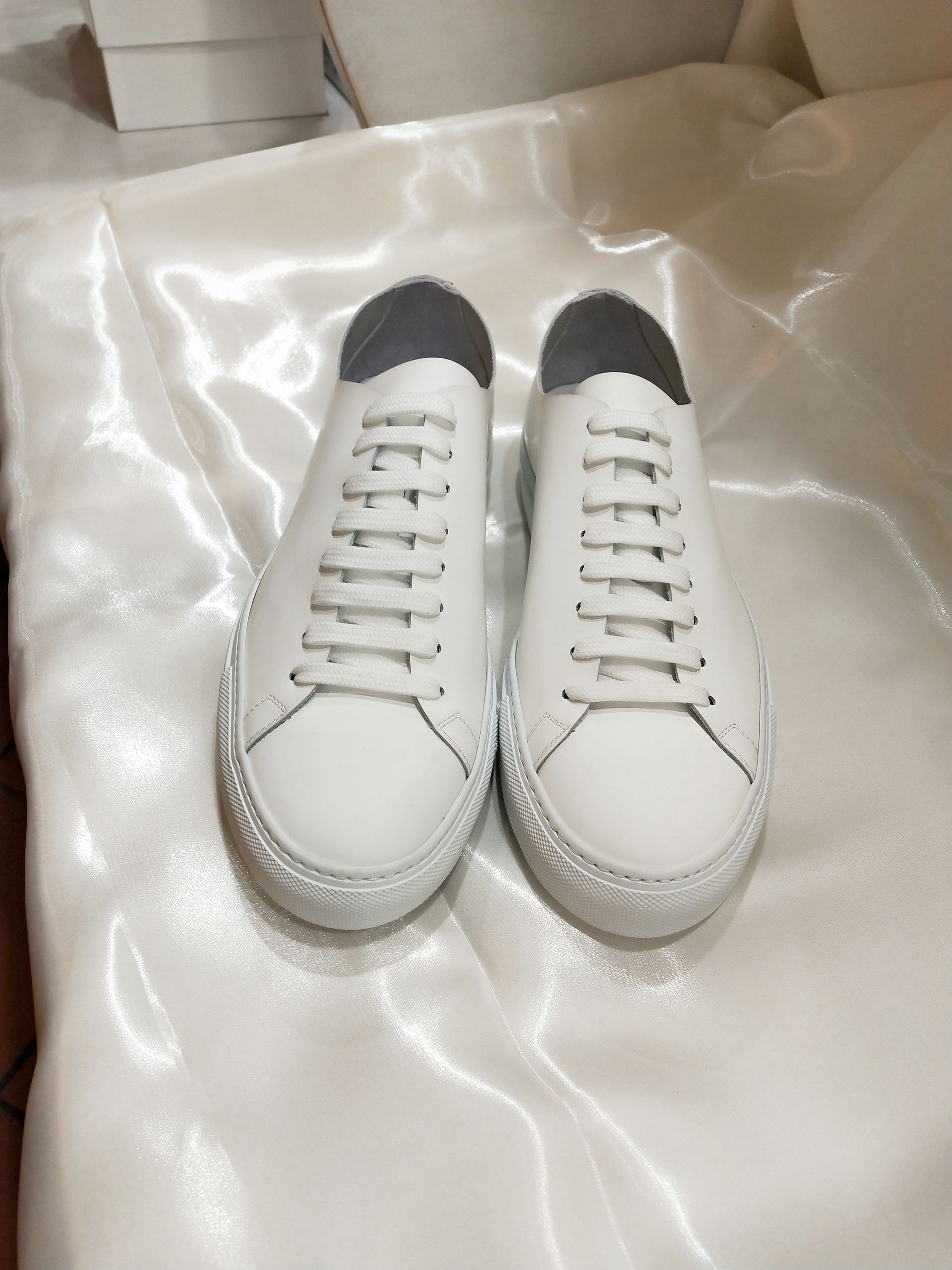 Un paio di scarpe da ginnastica in pelle bianca, esposte su una superficie drappeggiata di raso bianco.