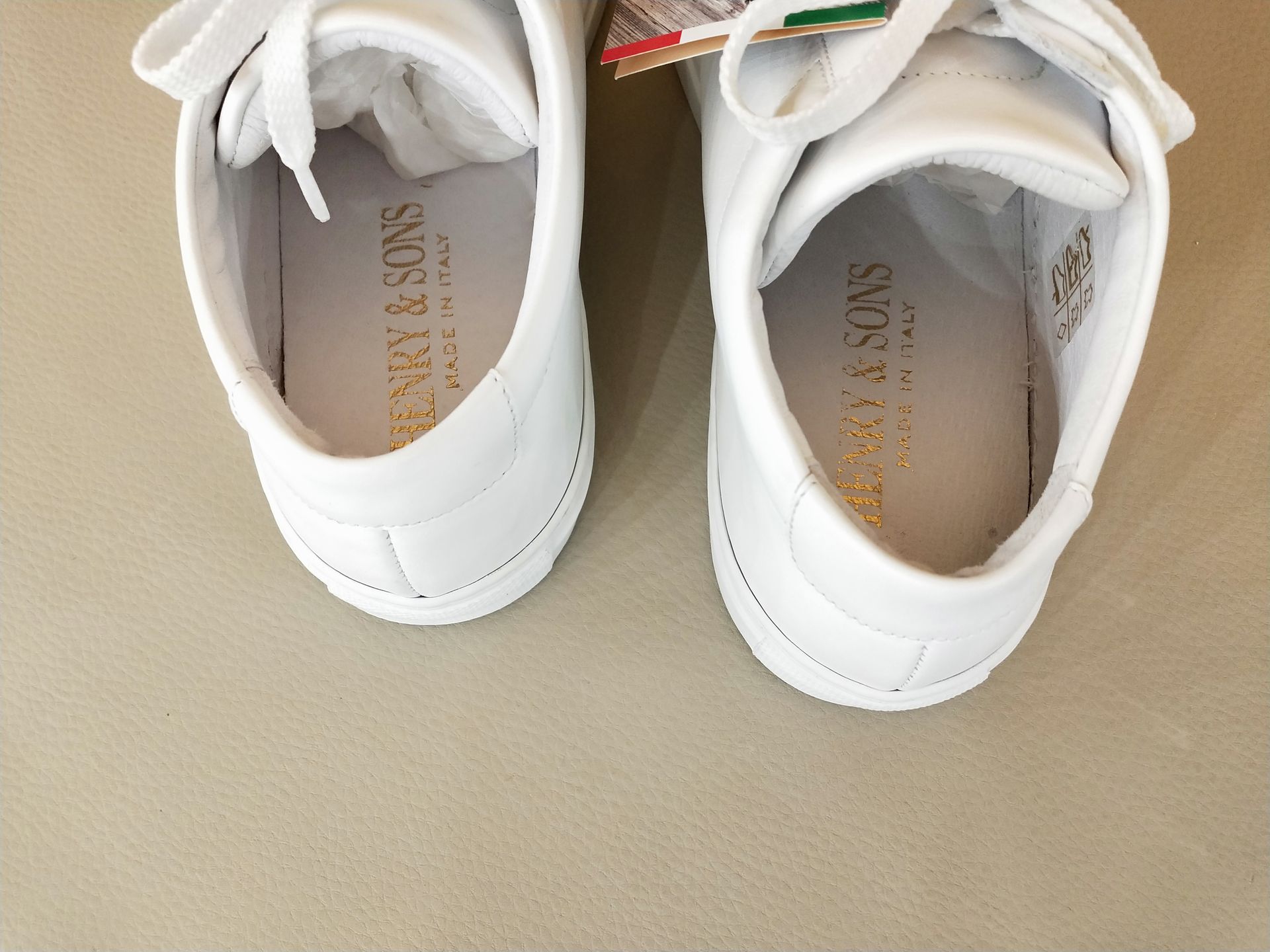 Vista dall'alto di un paio di scarpe da ginnastica in pelle bianca con logo dorato sulle solette, su uno sfondo neutro.