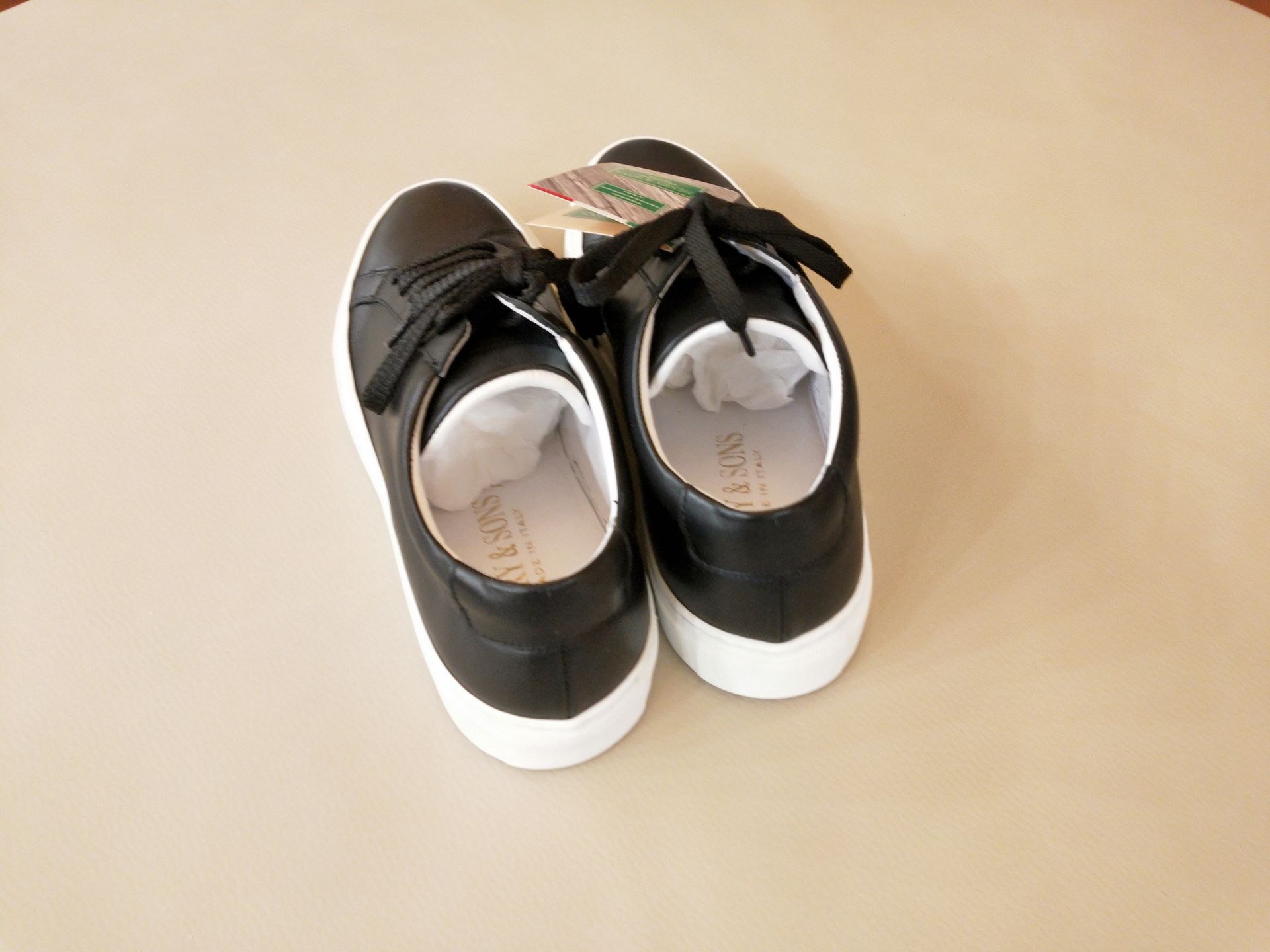 Un paio di scarpe da ginnastica nere con suola bianca e lacci neri, viste dall'alto su uno sfondo beige.