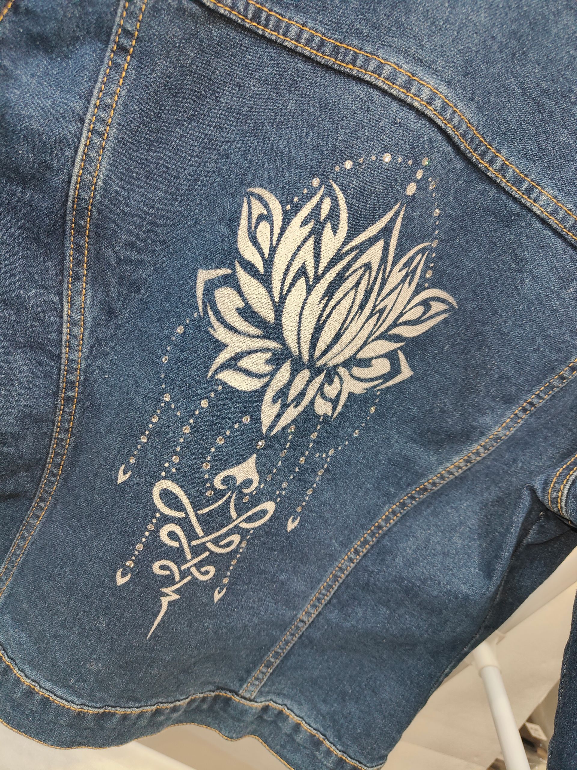 Sul retro di una giacca di jeans blu è stampato un disegno di un fiore di loto bianco con linee ornamentali pendenti.