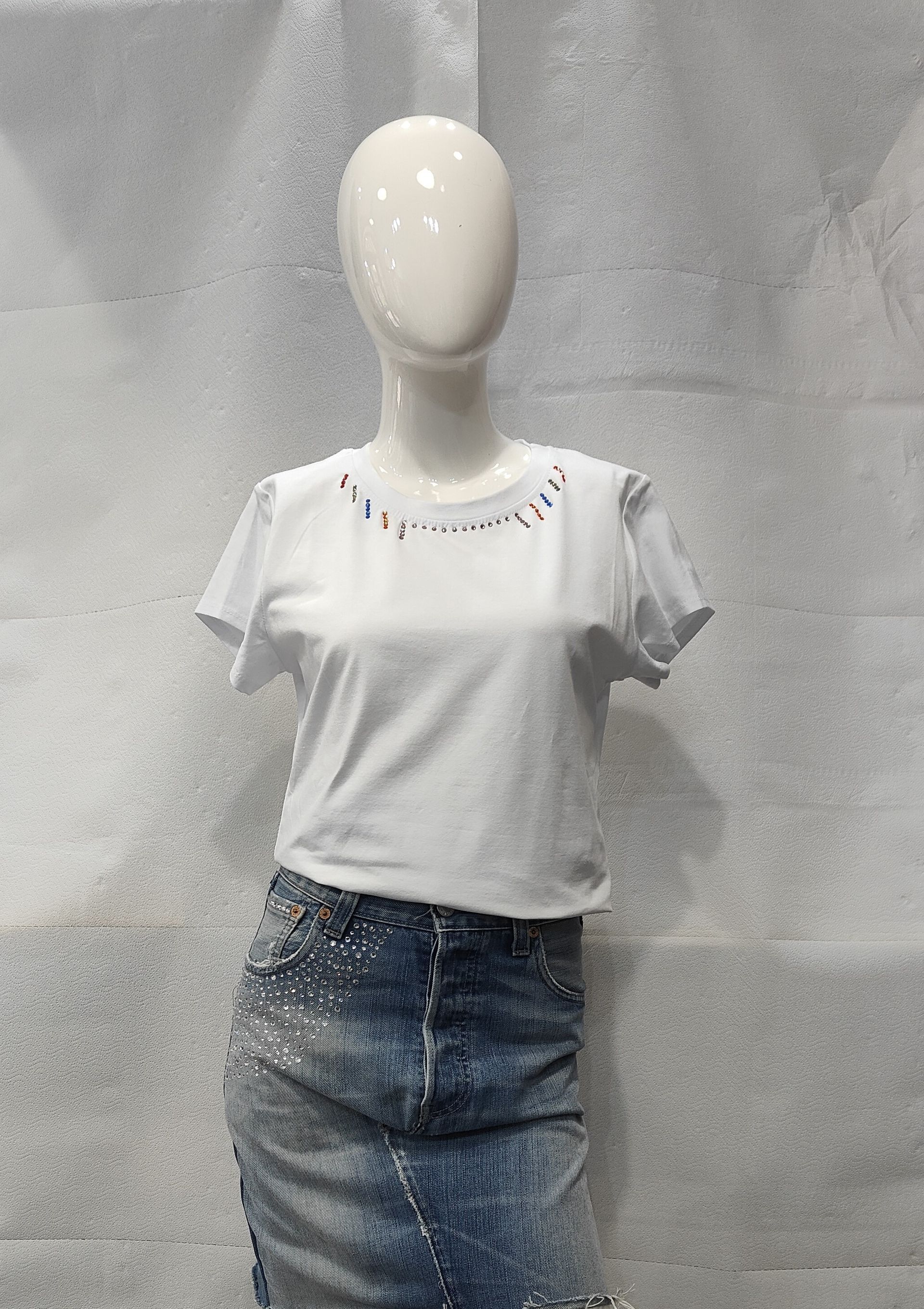 Un manichino indossa un top bianco a maniche corte con una scollatura decorata da perline e una gonna di jeans blu.