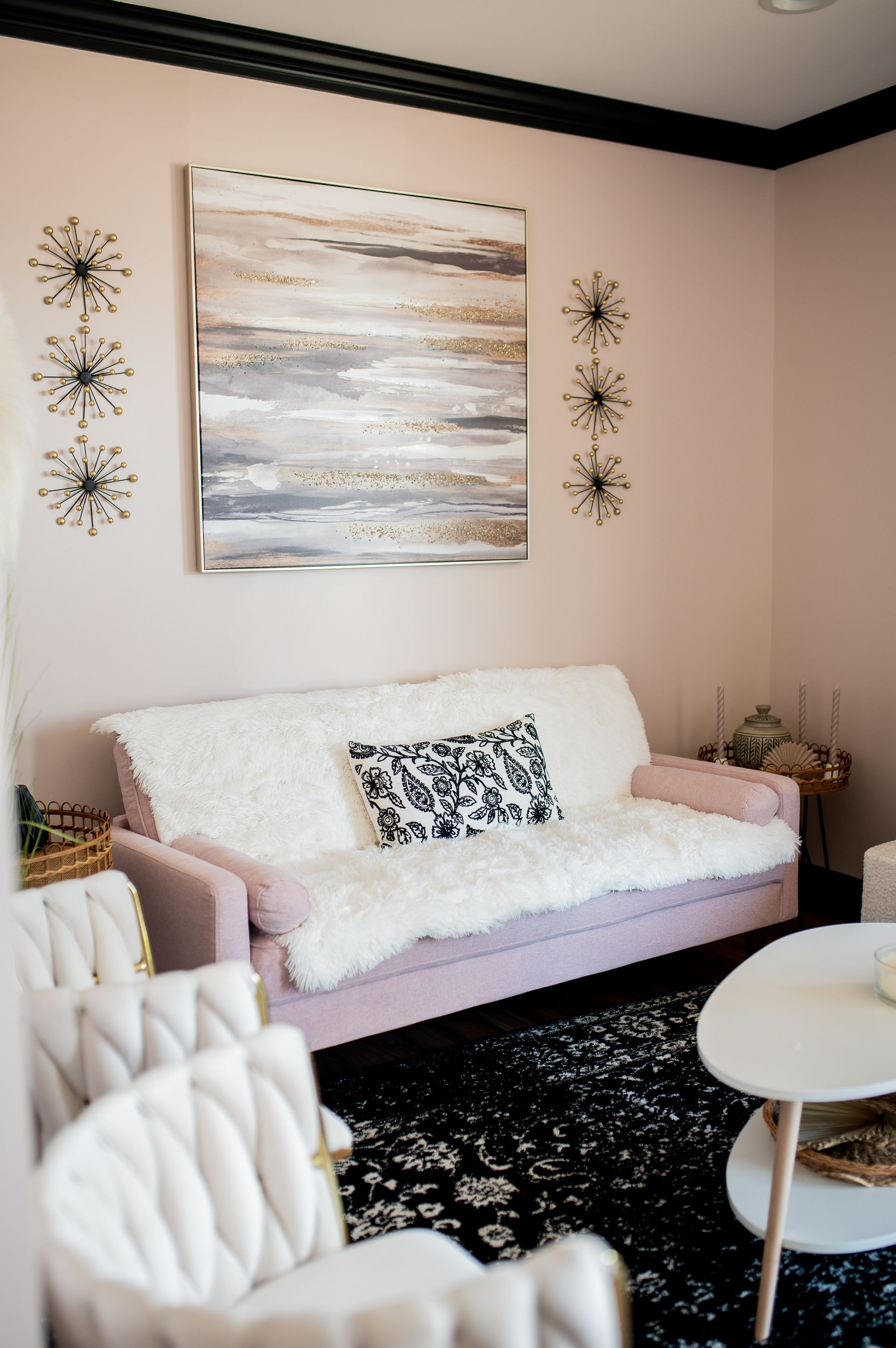 A living room with a pink couch , white chairs , a coffee table and a painting on the wall.