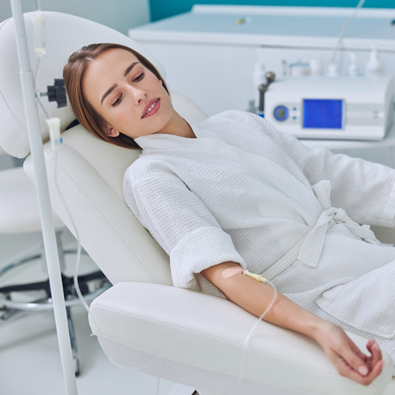 A woman is sitting on a bed with an iv in her hand.