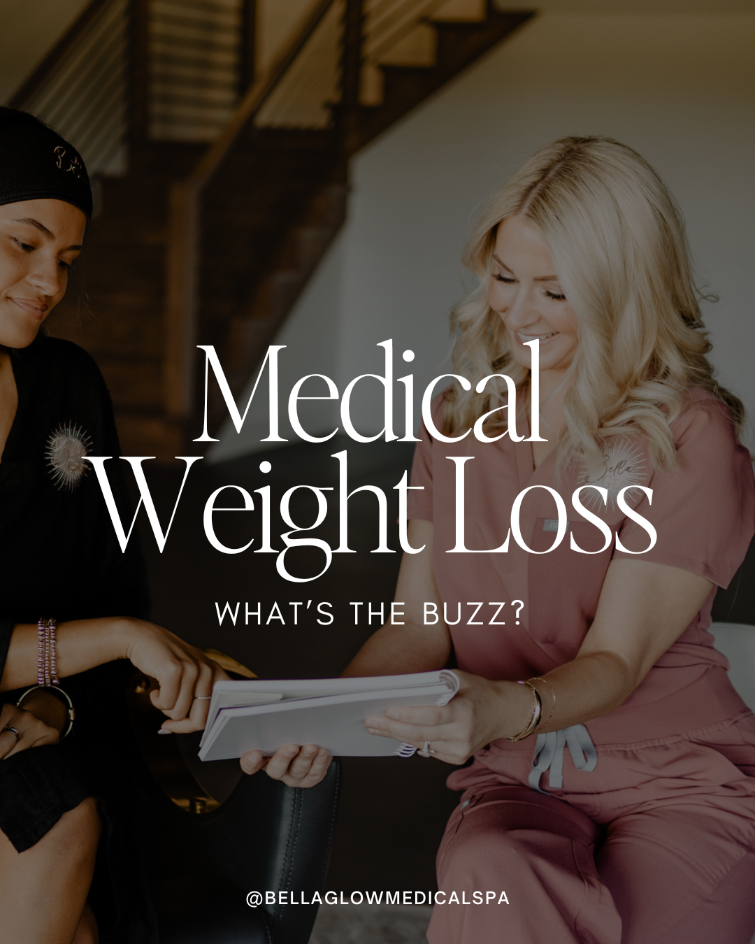 Two women looking at tablet; one wearing medical scrubs, other in dark clothing.