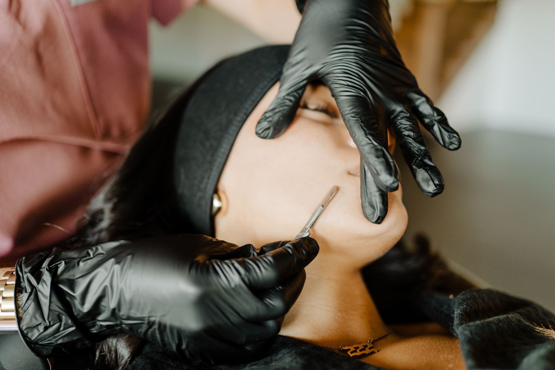 Person receiving lip treatment with gloved hands holding tools.