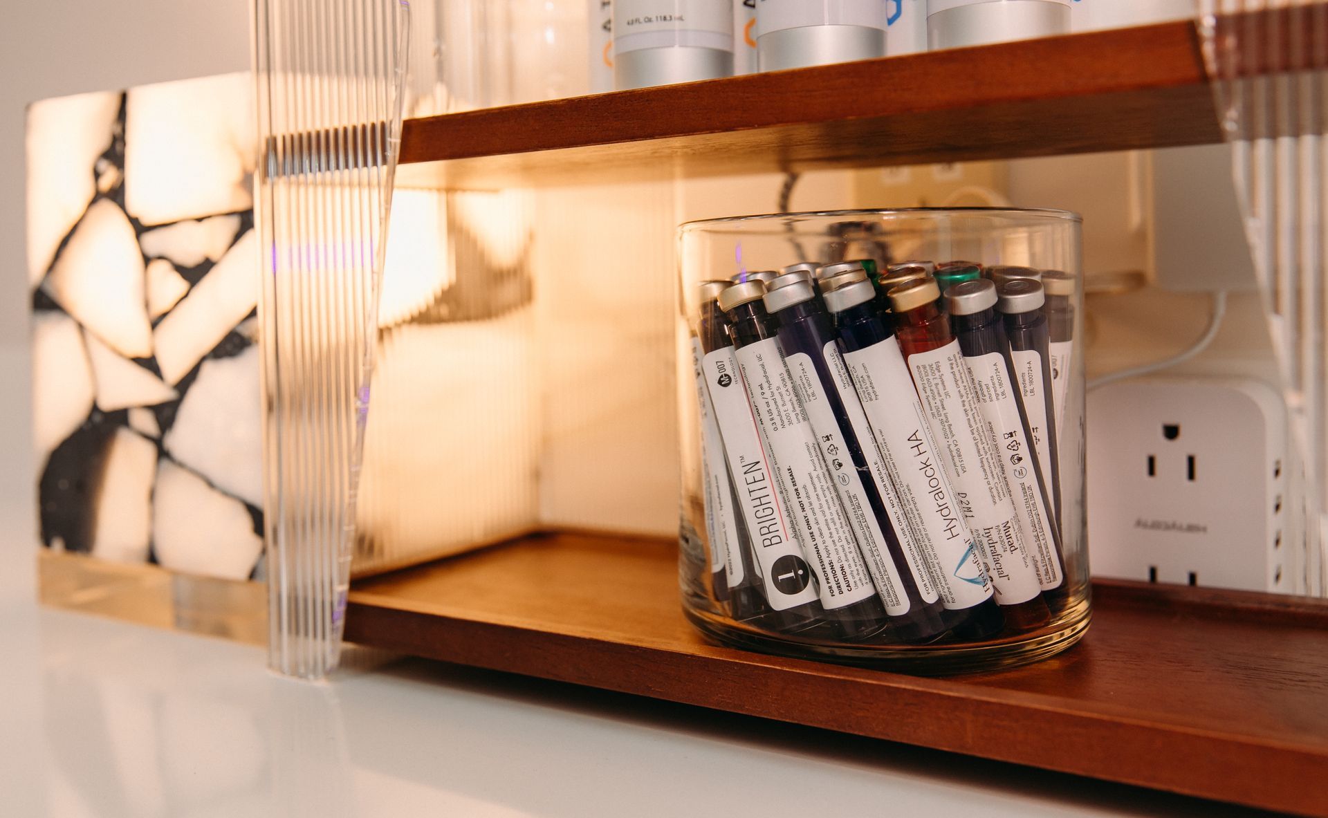 A glass filled with colored pencils is on a wooden shelf.