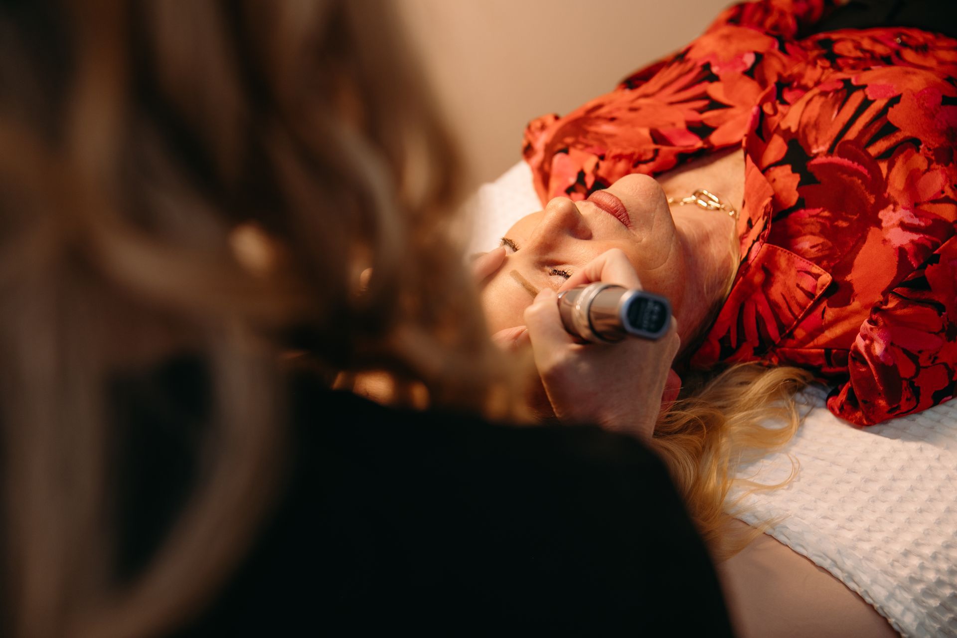 A woman is laying on a bed getting a treatment on her face.