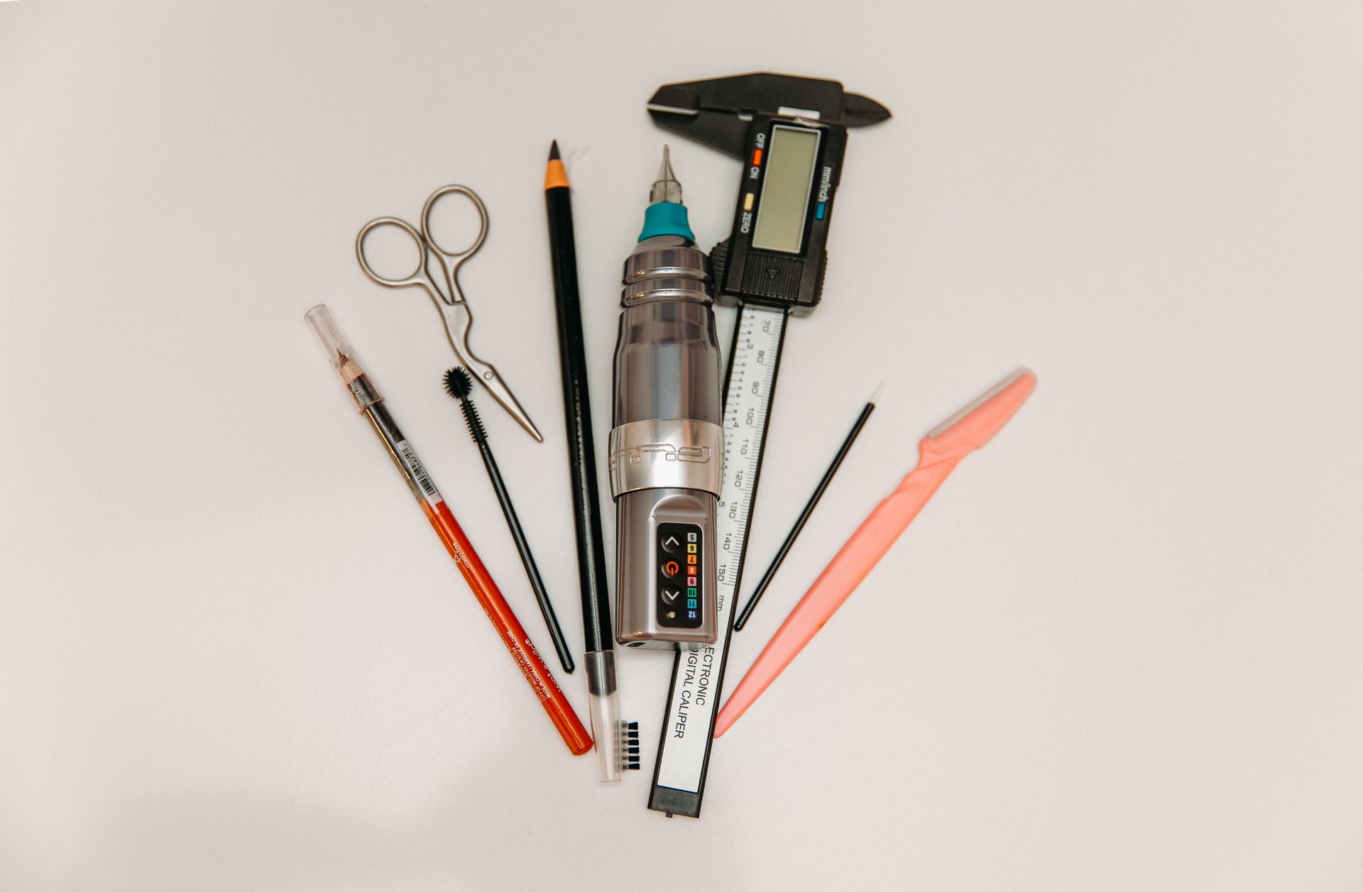 A bunch of pencils , scissors , a ruler , and a digital caliper on a white surface.