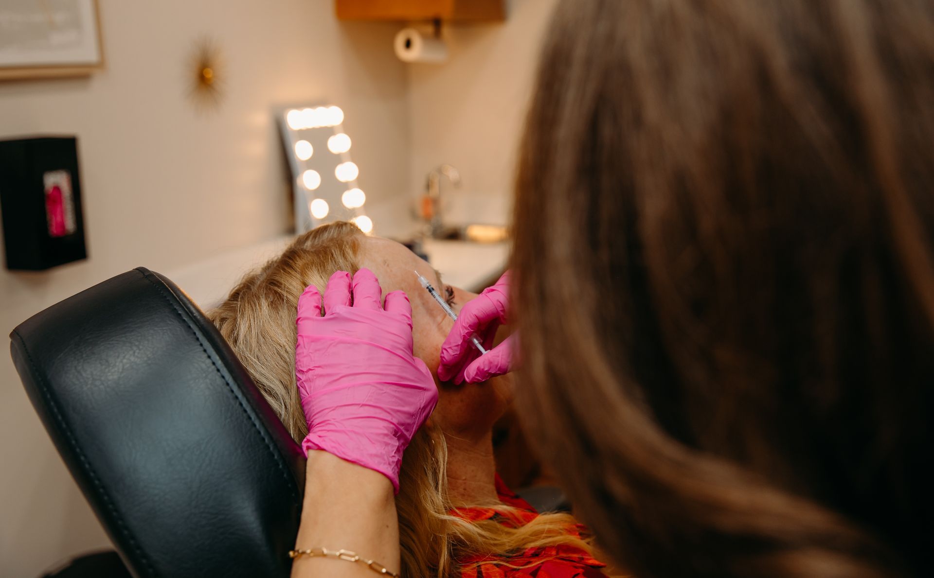 A woman wearing pink gloves is holding a syringe.