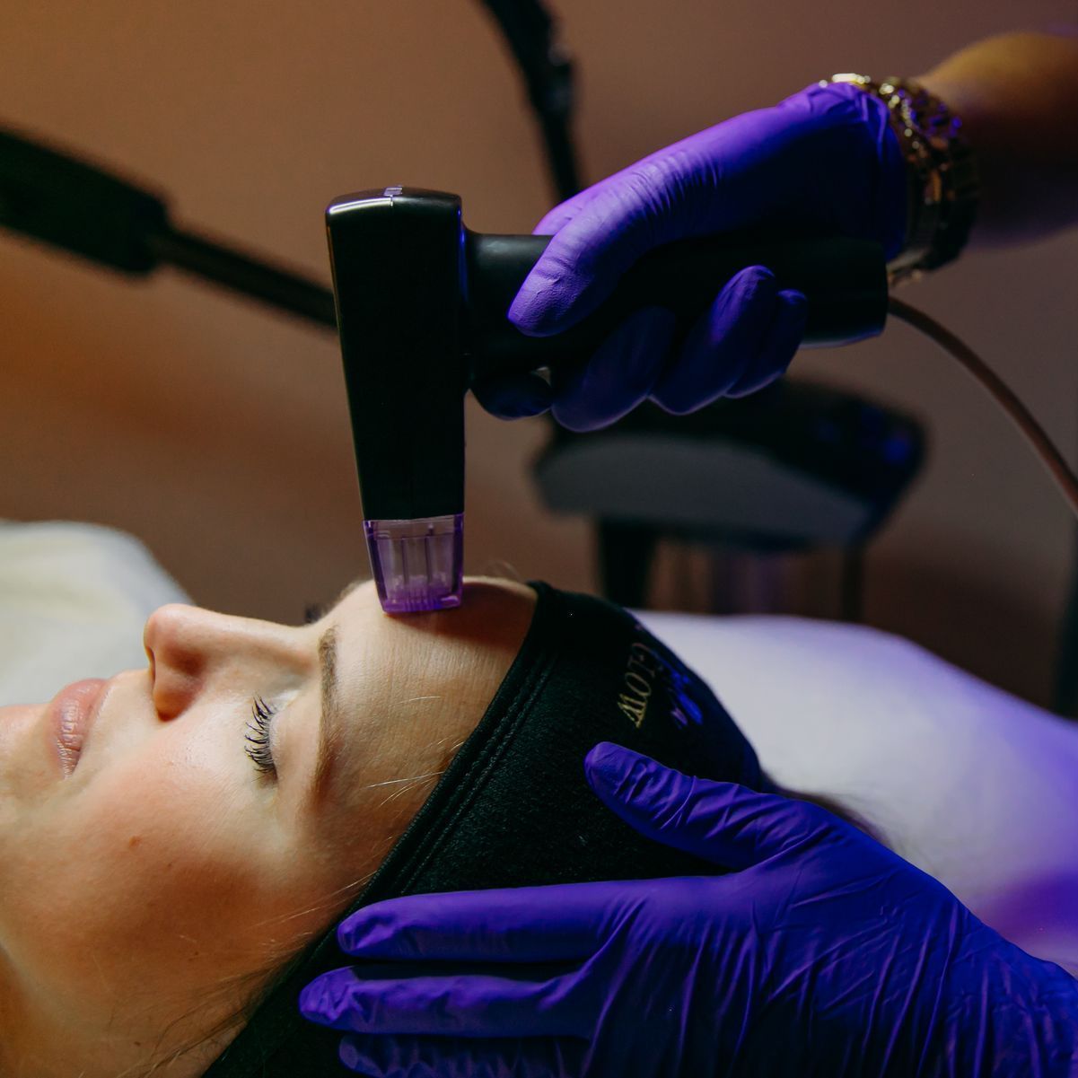 A woman is getting a treatment on her face with purple gloves.