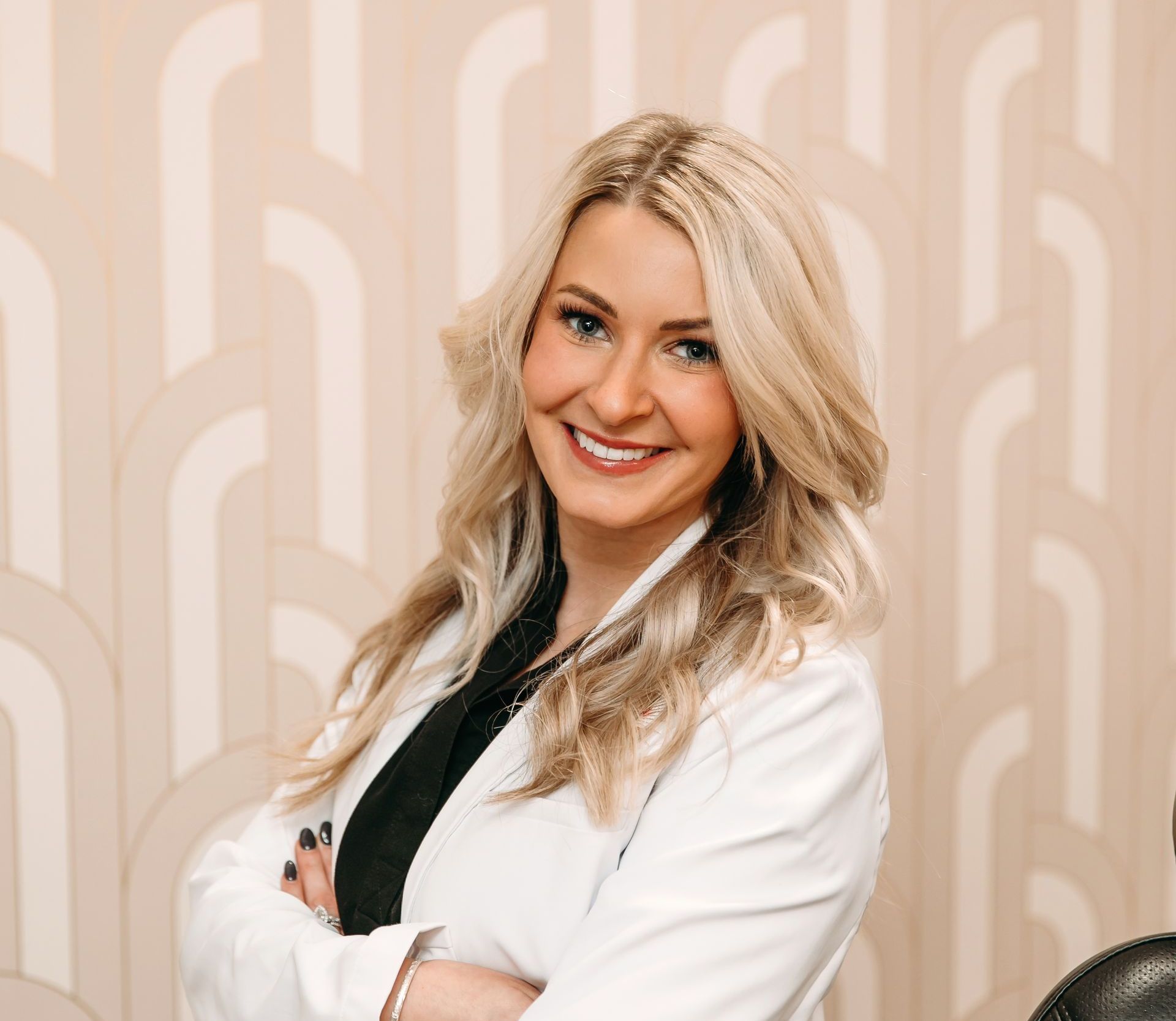 A woman in a white coat is smiling with her arms crossed.