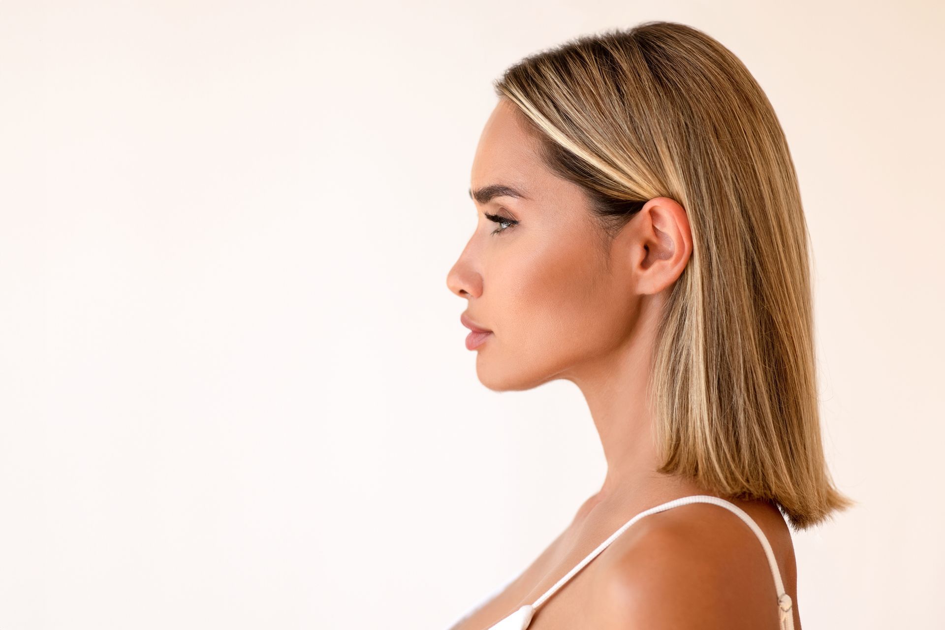 A woman with blonde hair is wearing a white tank top.