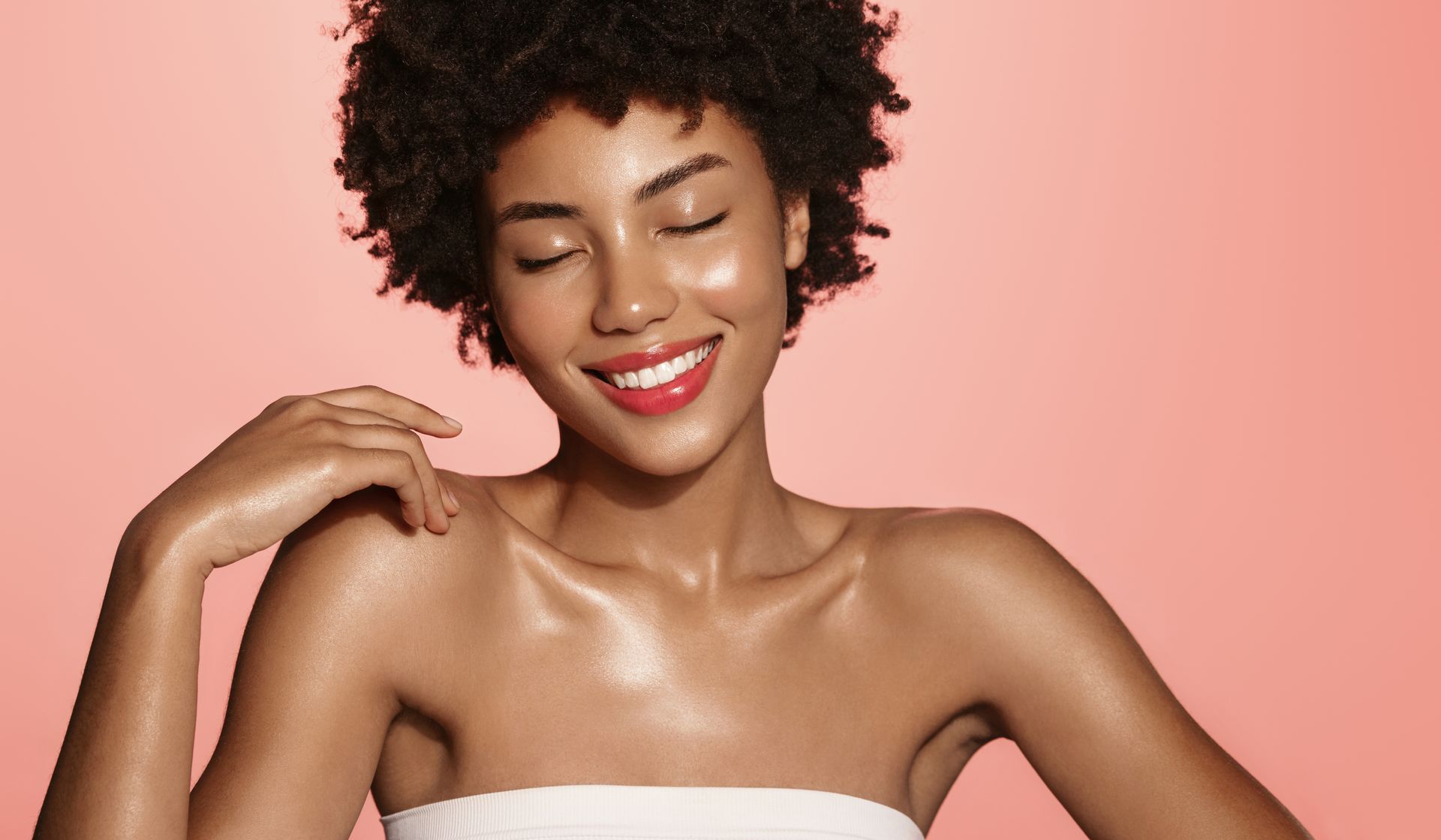 A woman is smiling with her eyes closed and her hand on her shoulder.