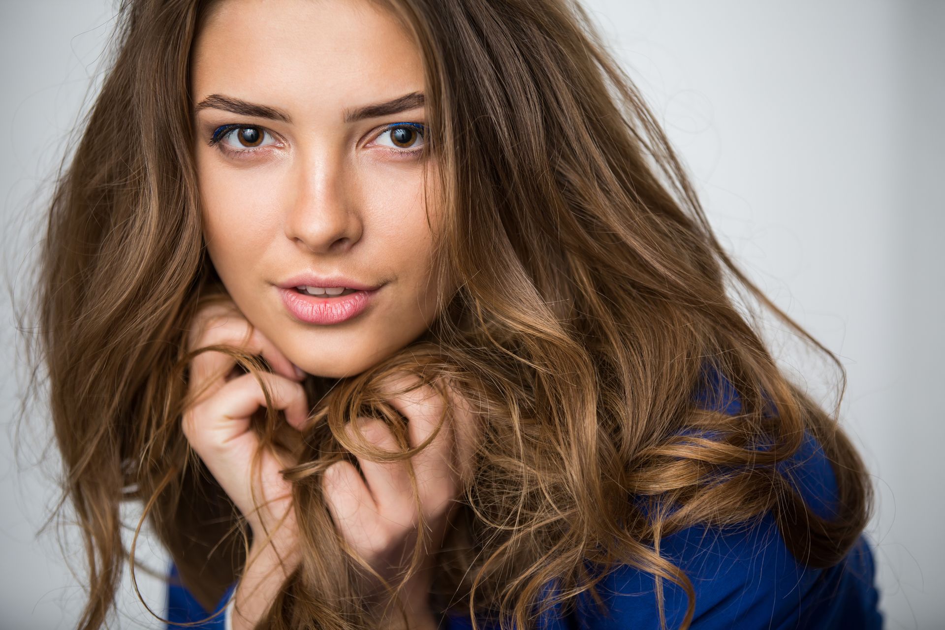 The woman is wearing a blue sweater and holding her hair in her hands.