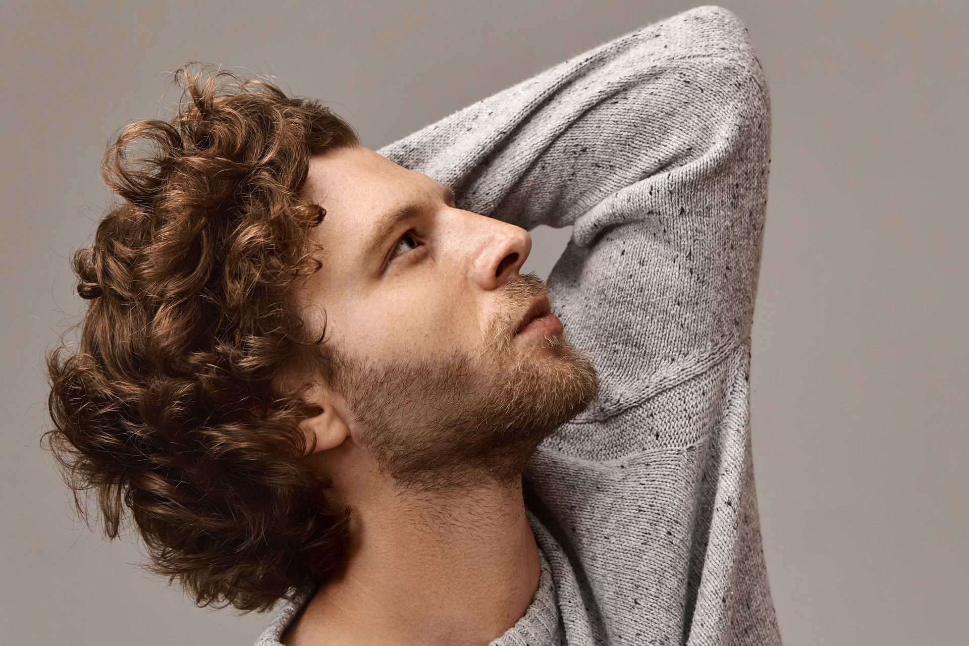 A man with curly hair and a beard is wearing a grey sweater.