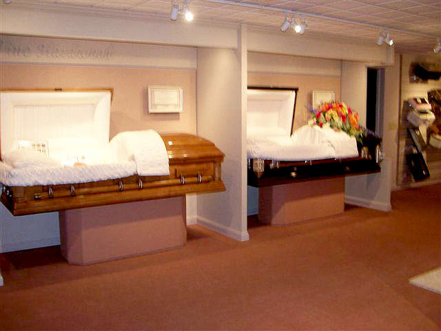 Two open coffins displayed in a funeral home, one with a floral arrangement.