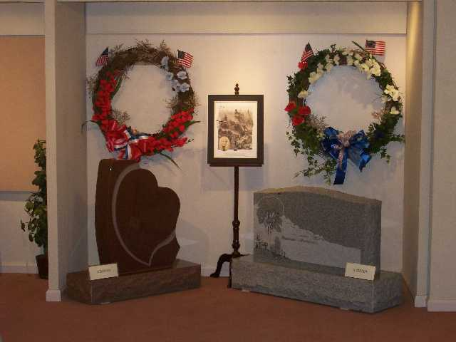 Memorial display with two wreaths, tombstones, and a framed photo.