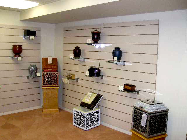 A display room with various cremation urns on shelves against neutral-colored walls and carpeting.