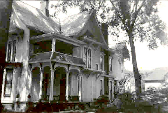 Gothic Victorian house with porch and ornate details, trees, and sky visible.