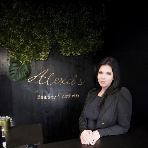 Eine frau sitzt an einer theke vor einem schild mit der aufschrift „alexas schönheit und ästhetischkeit“.