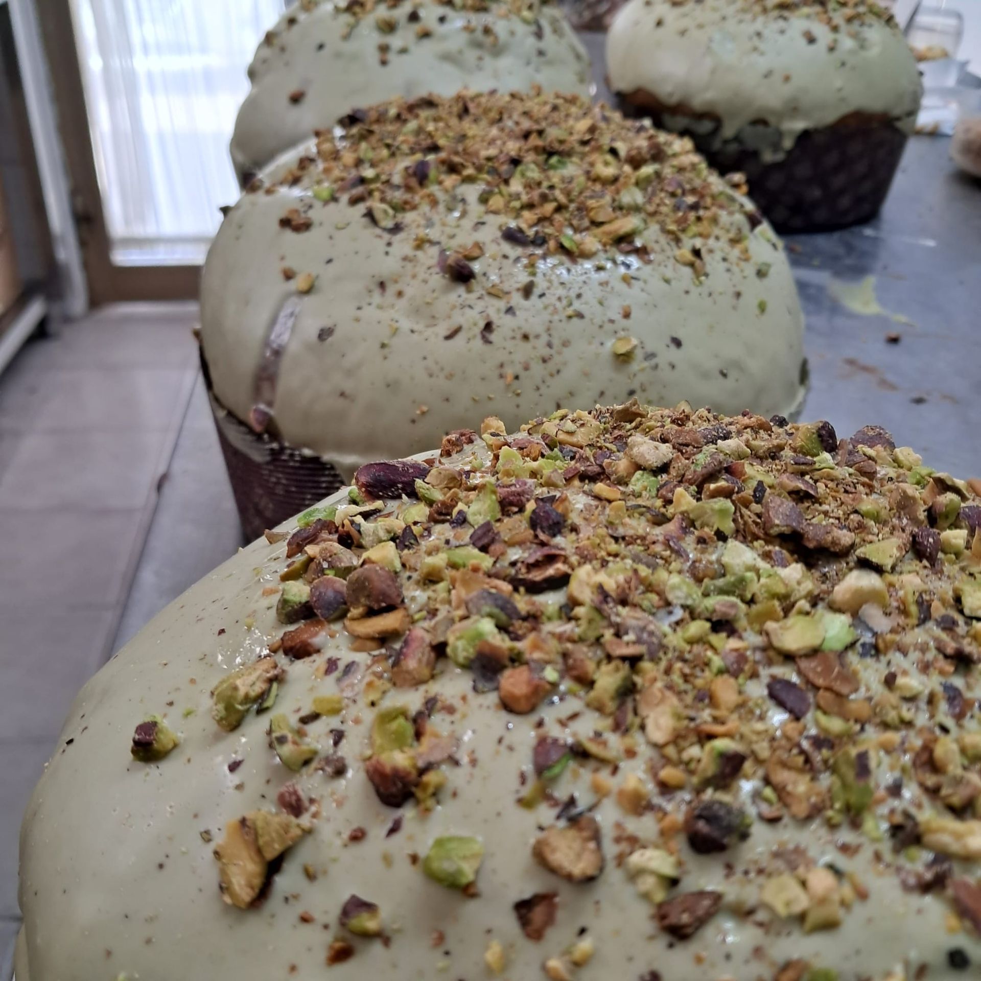 Primo piano di prodotti da forno ricoperti di pistacchi, glassati di verde chiaro e con noci tritate, allineati su un tavolo.