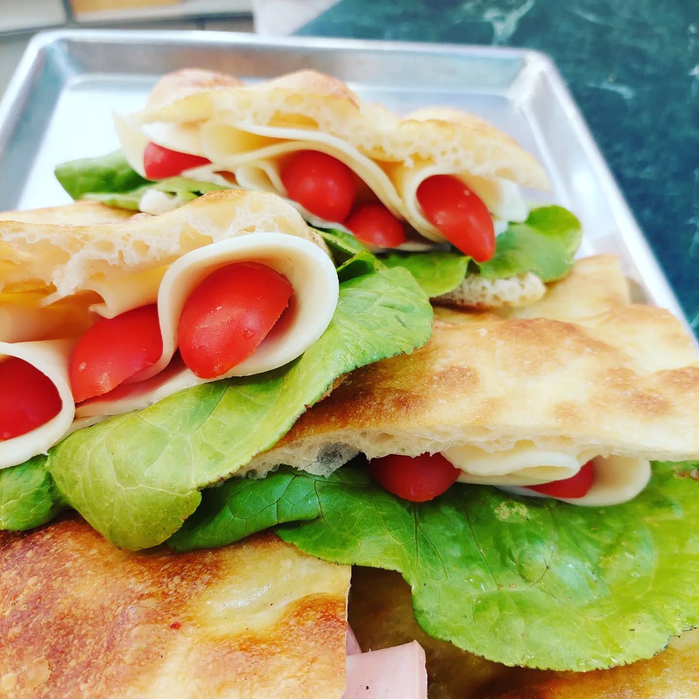 Panino fatto con focaccia, prosciutto cotto, mozzarella, pomodorini e lattuga.