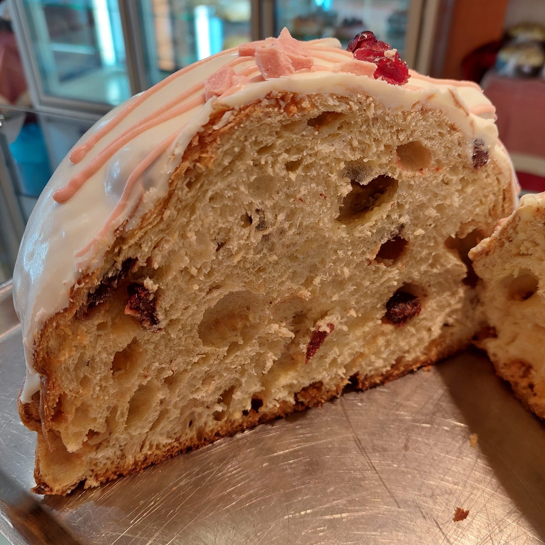 Sezione trasversale di un pane glassato alla crema con frutta secca incorporata, glassa rosa e bacche rosse sulla superficie.