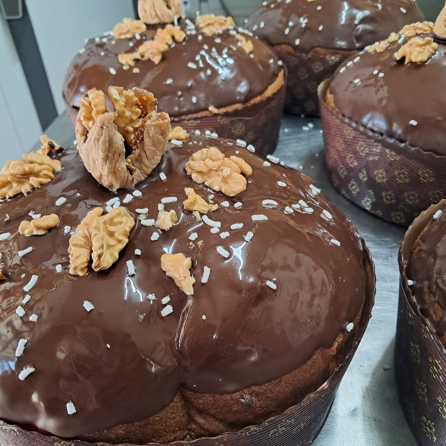 Tortine rotonde ricoperte di cioccolato, noci e granella su una superficie metallica.