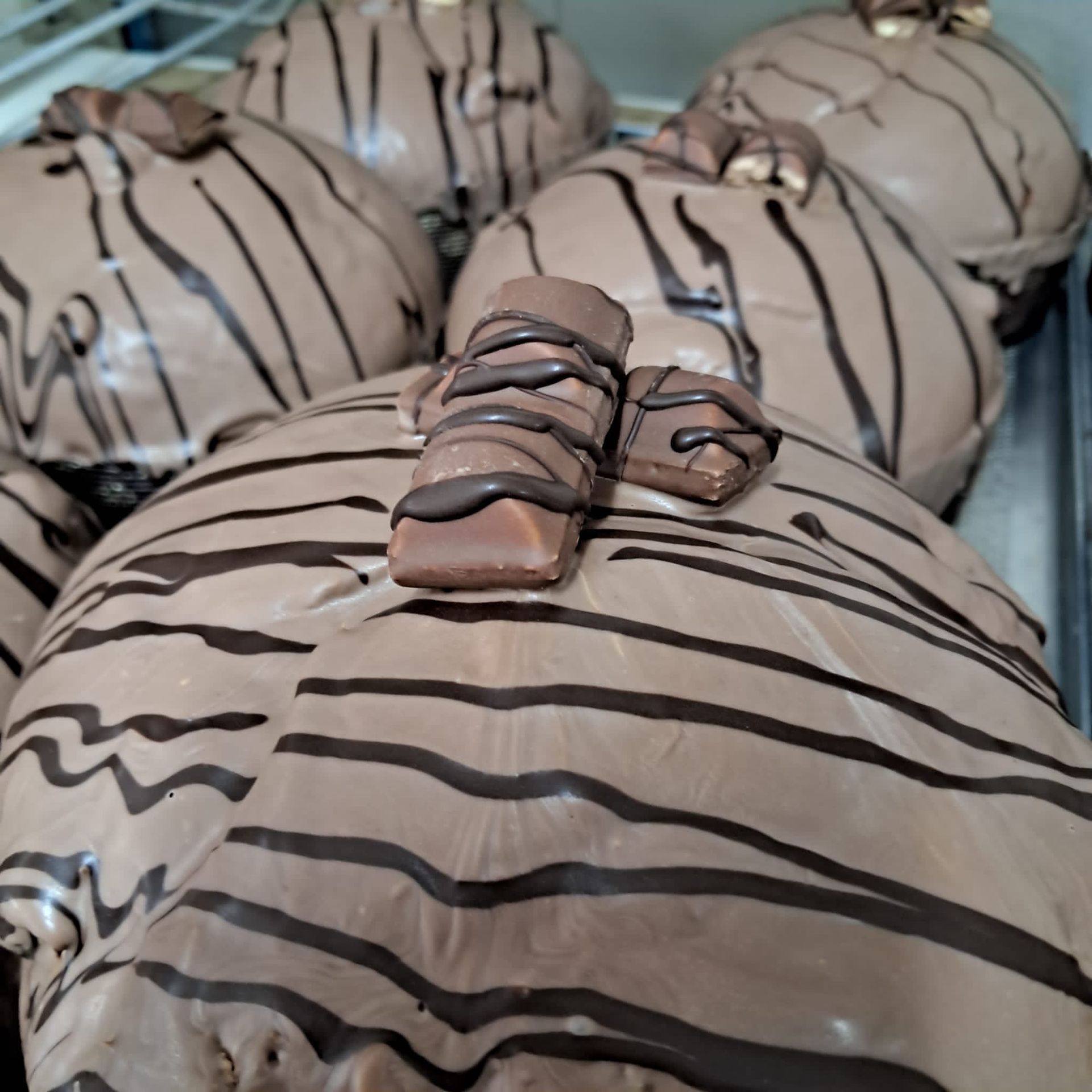 Ciambelle ricoperte di cioccolato con strisce di cioccolato ricoperte e mini pezzi di tavoletta di cioccolato sopra.