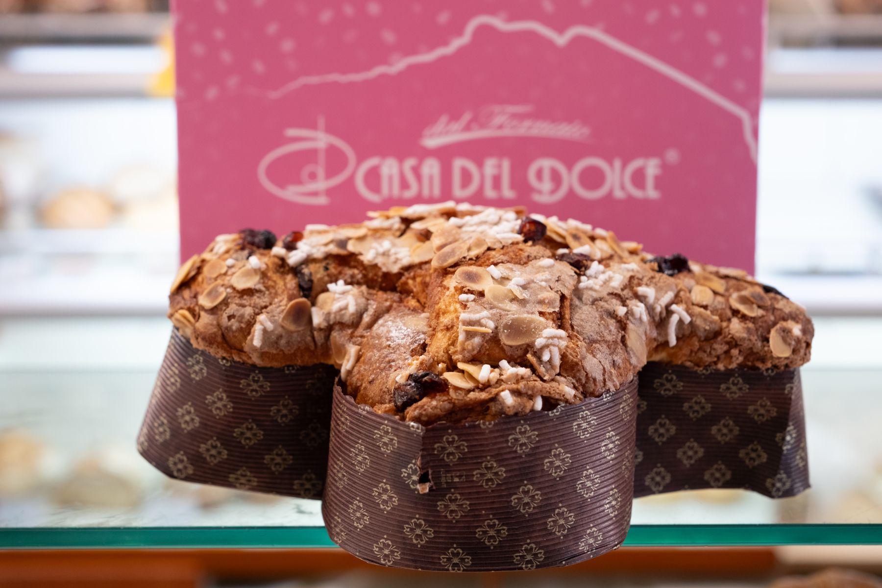 Una colomba a forma di colomba con noci e cioccolato, esposta in una pasticceria con un'insegna rosa.