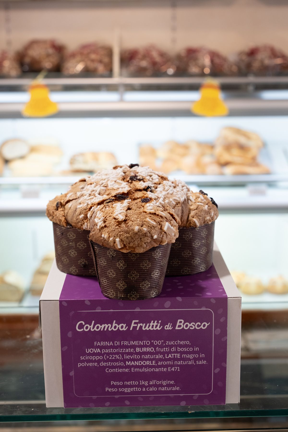 Colomba ai frutti di bosco esposta in una vetrina da pasticceria. Scatola viola con testo.