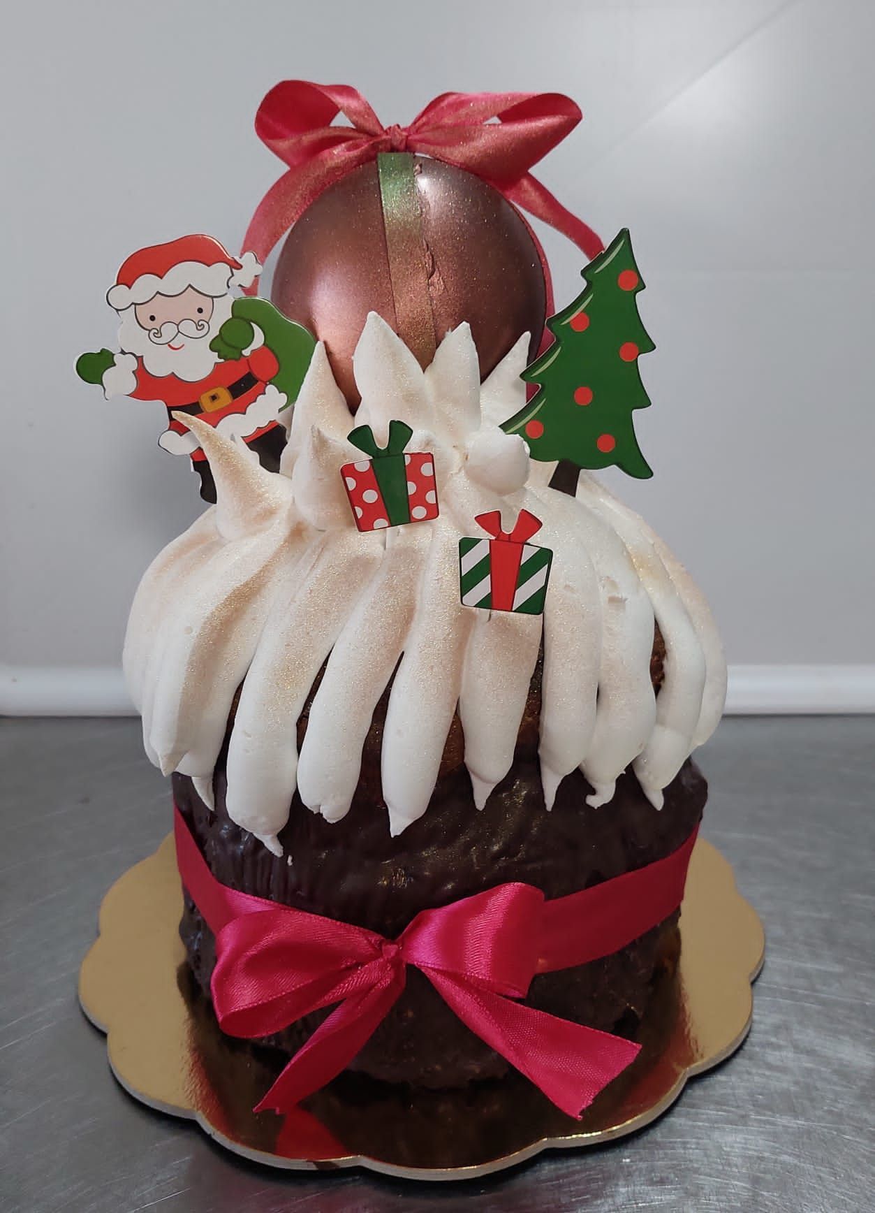 Torta a tema natalizio con glassa bianca, decorazioni a forma di Babbo Natale e albero, guarnita con un fiocco.